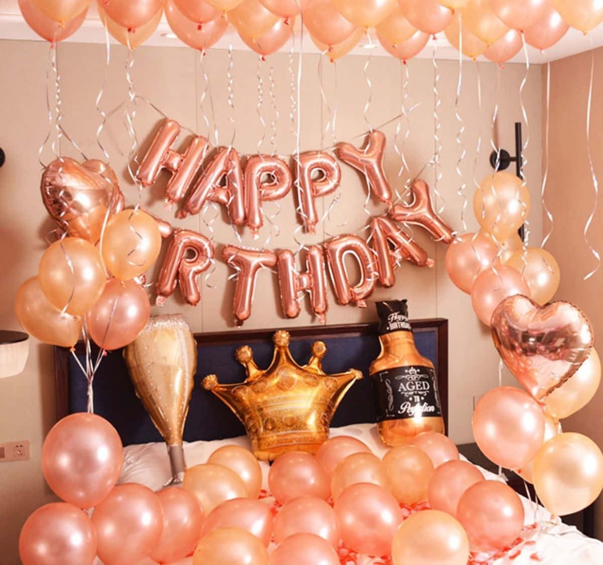 與親友一同慶祝你的生日！ 壁紙 — 一張床，點綴著玫瑰金色氣球和「HAPPY BIRTHDAY」橫幅，周圍環繞著派對裝飾。