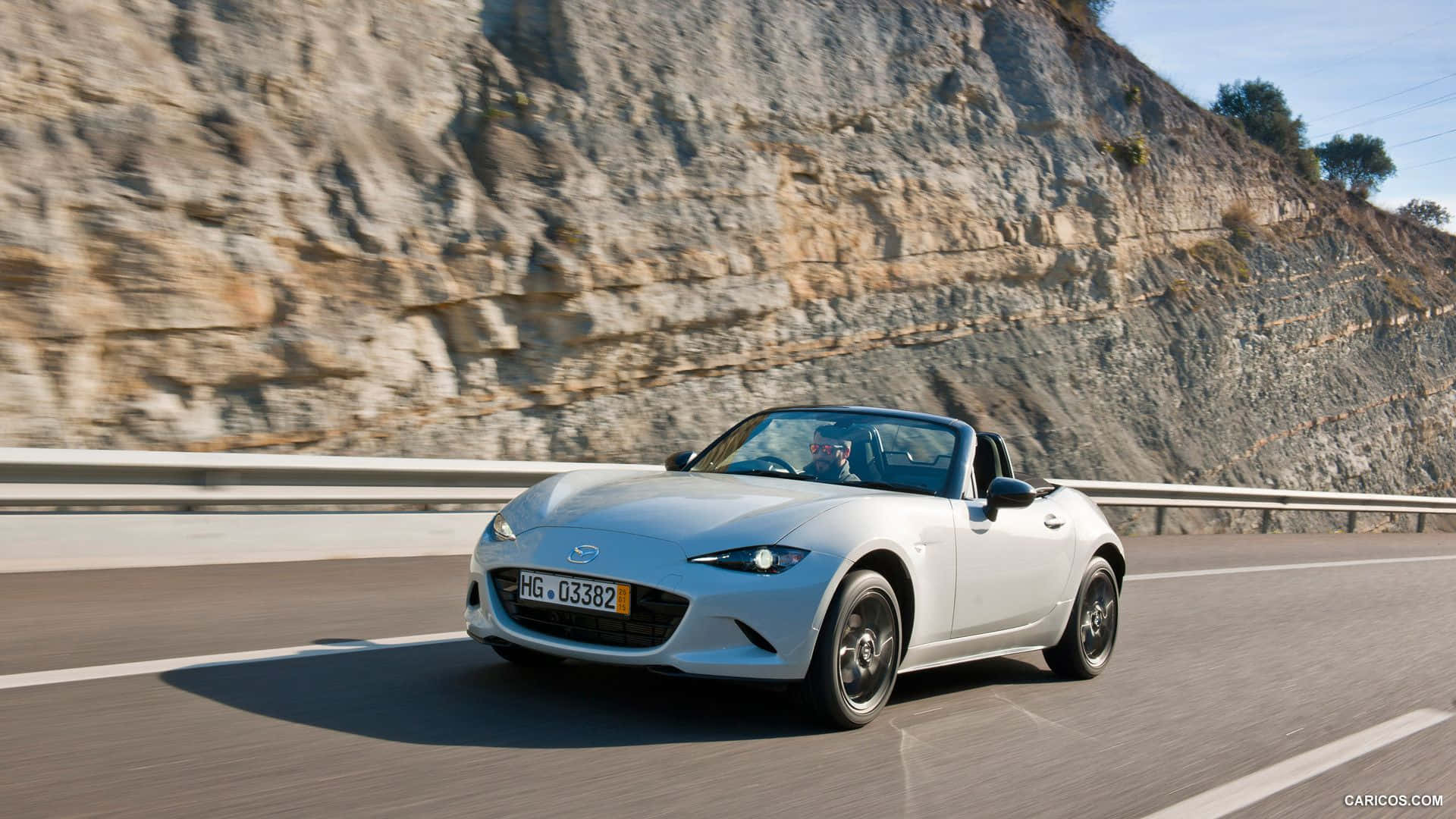 與馬自達MX-5 Miata共享迎風駕馭的自由 壁紙 — 一輛銀色開篷跑車沿著蜿蜒的山路飛馳，背景是崎嶇的懸崖峭壁。
