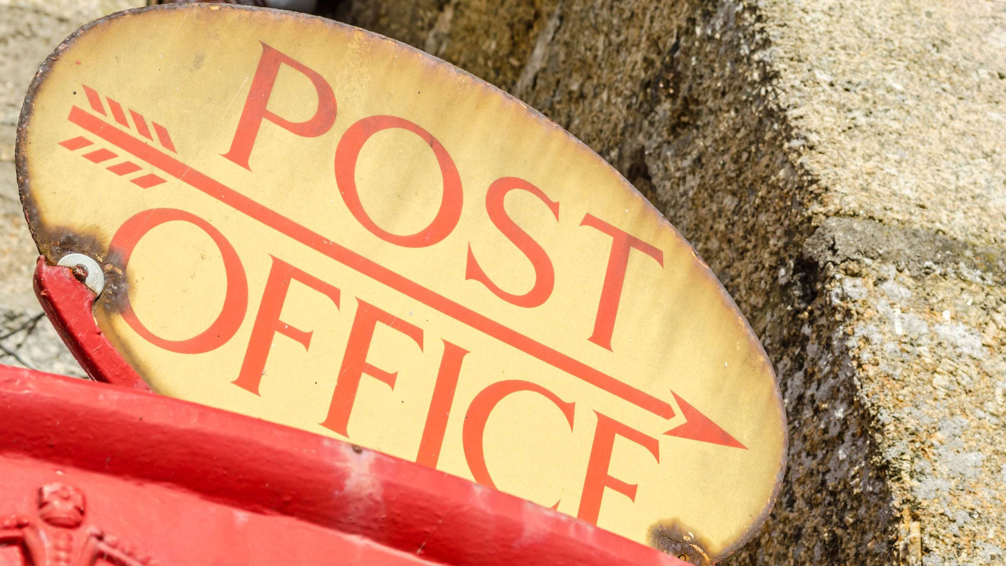 舊郵政局招牌 壁紙 — 一個風化的黃色橢圓形標誌，帶有紅色「POST OFFICE」文字和指向右邊的箭頭，靠在粗糙的石牆上。