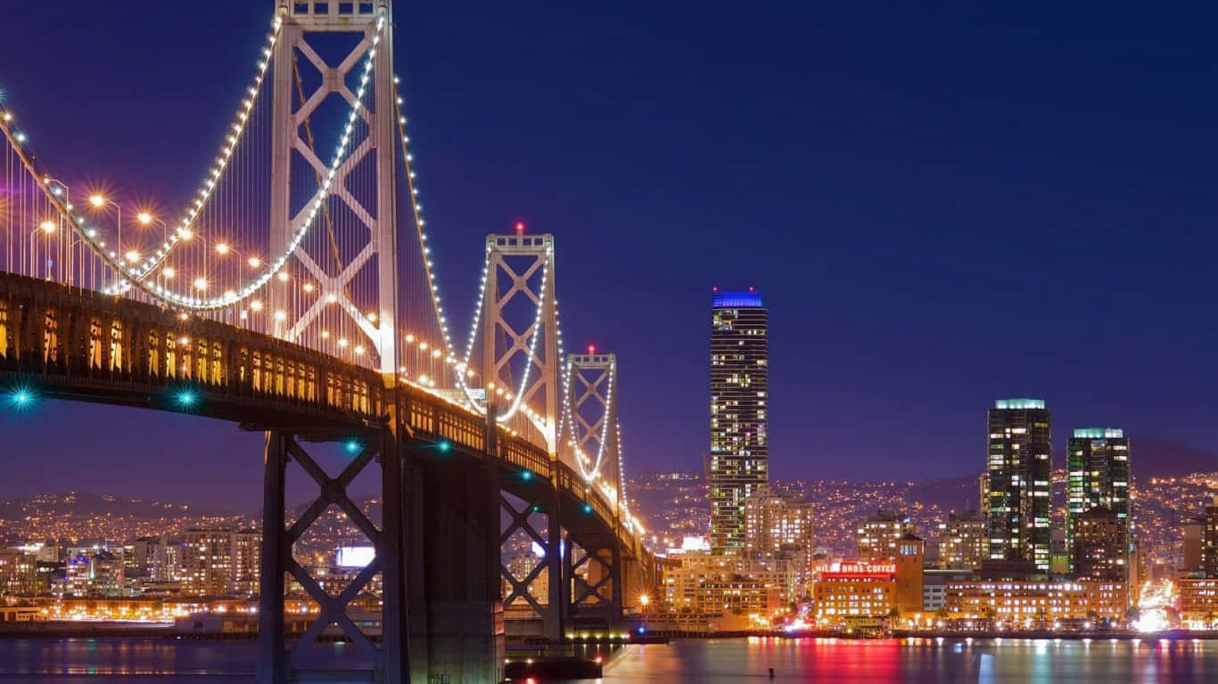 夜晚燈光璀璨的灣區大橋和三藩市天際線，城市燈光倒映在水面上。