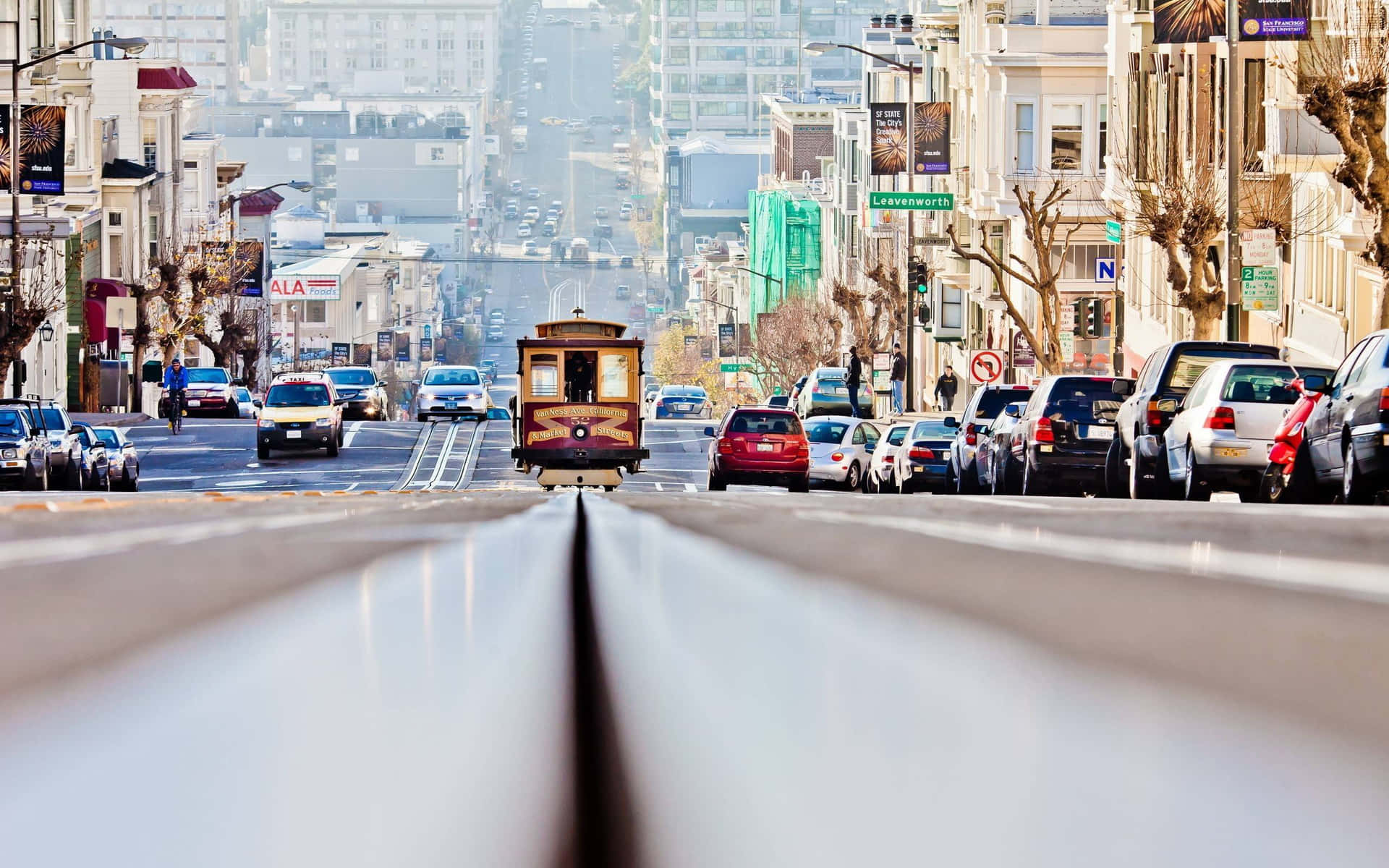 一輛纜車爬上一條陡峭的城市街道，兩旁停有汽車和建築物。