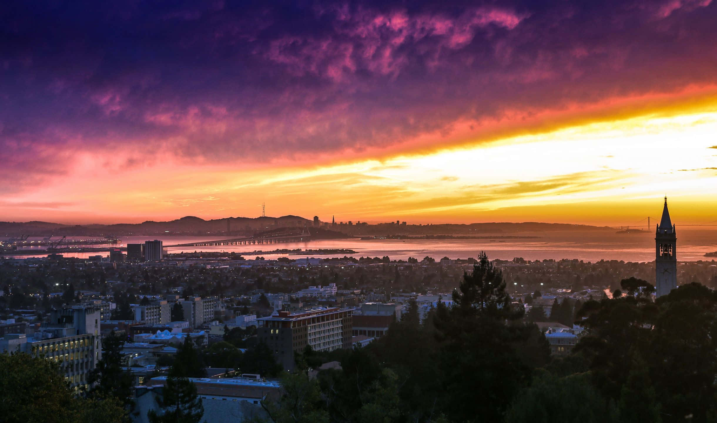 舊金山灣區夕陽美景 壁紙 — 令人驚嘆的日落將三藩市的天際線染成火熱的橙色和深紫色，遠處的金門大橋閃閃發光。