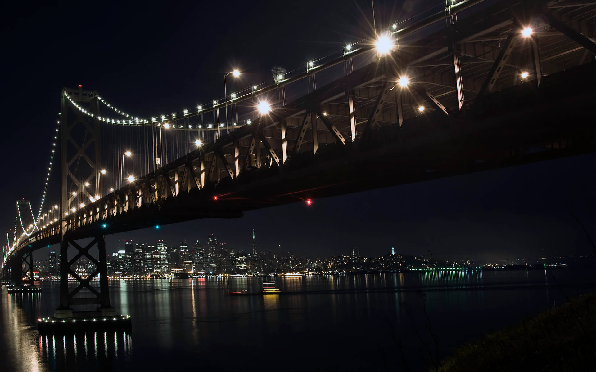 夜間背景中城市燈光映襯下，一座燈火通明的吊橋橫跨水面。