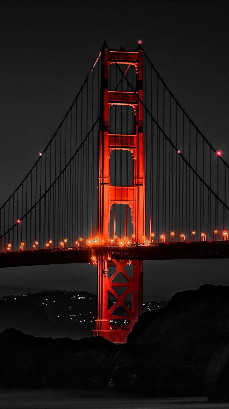 夜晚的金門大橋，周圍黑暗，遠處有城市燈光。