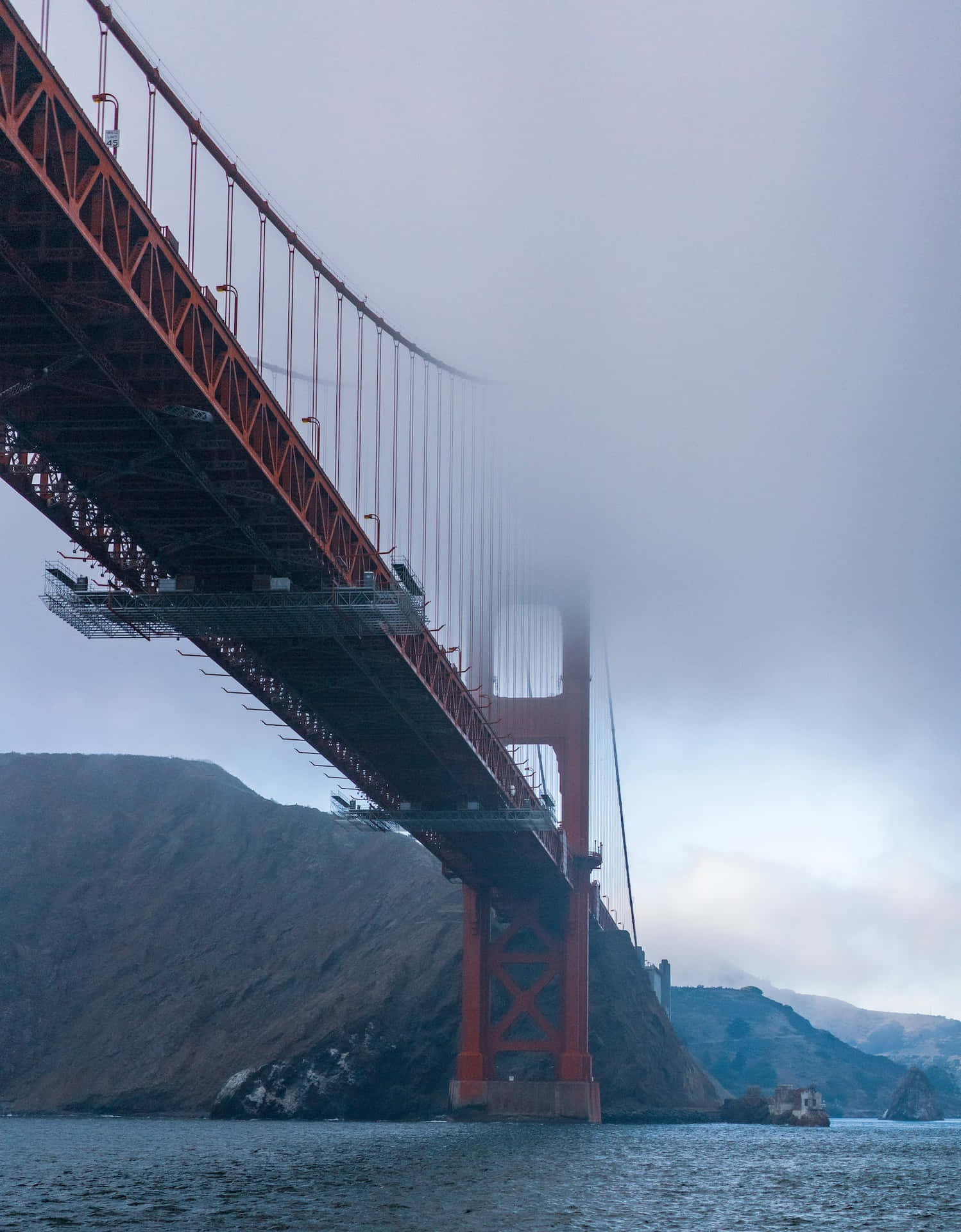 金門大橋部分被霧遮擋，下方是水面，背景有山丘