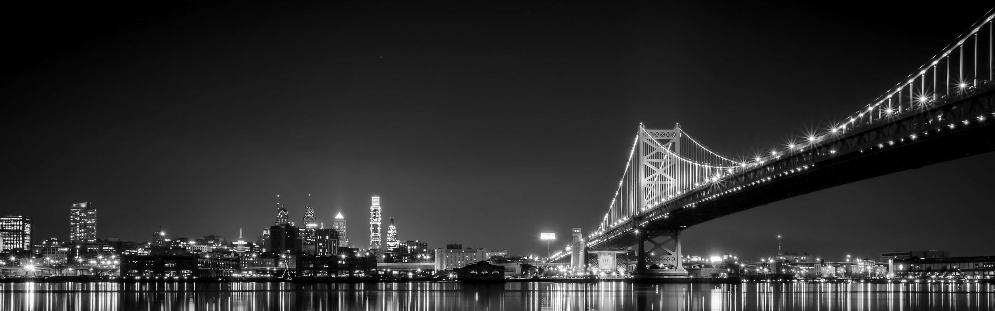 海灣大橋和三藩市天際線的黑白夜景，城市燈光倒映在水面上。