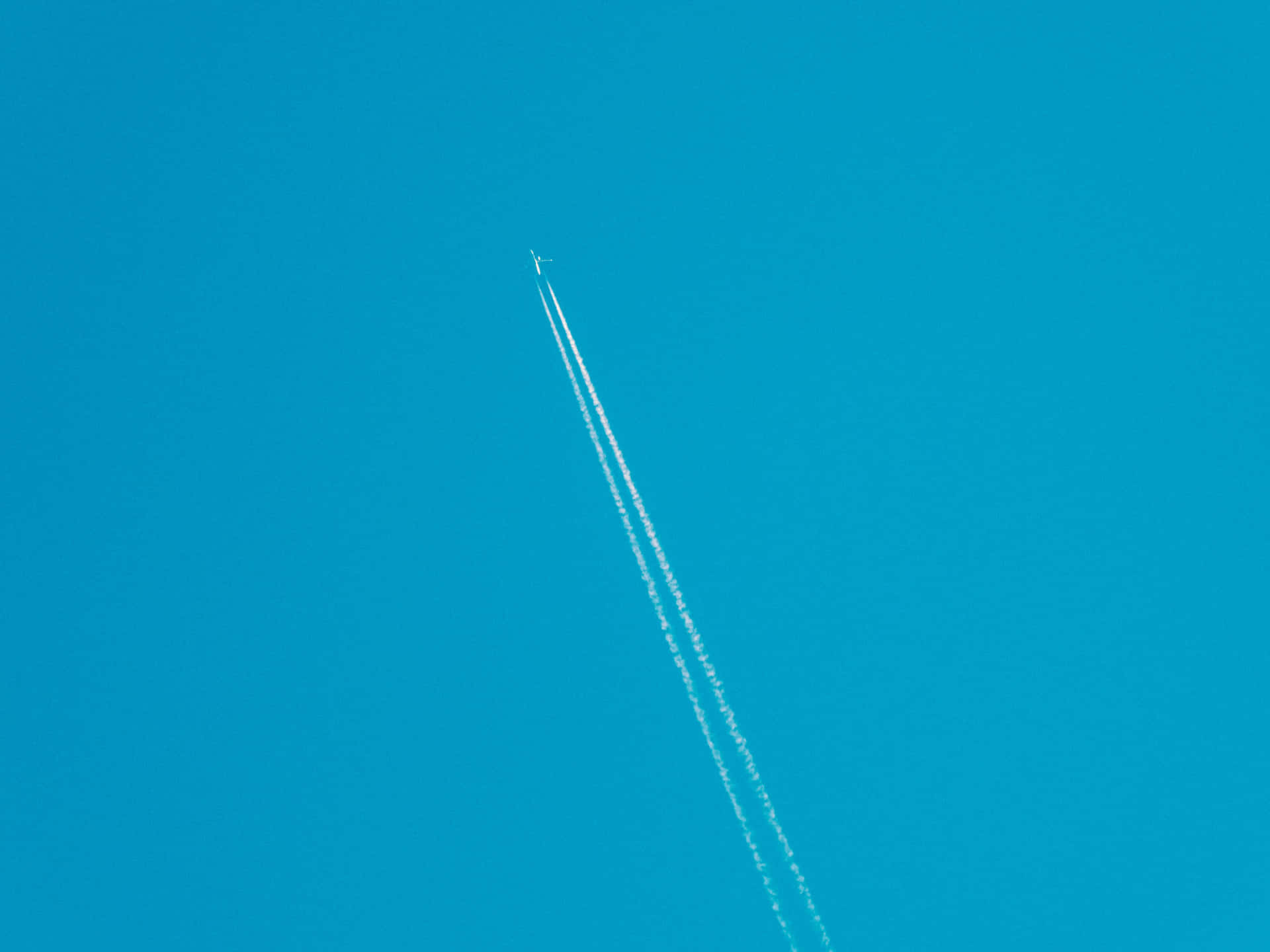 一架飛機在高空飛行，在明亮的藍天上留下兩道白色痕跡。