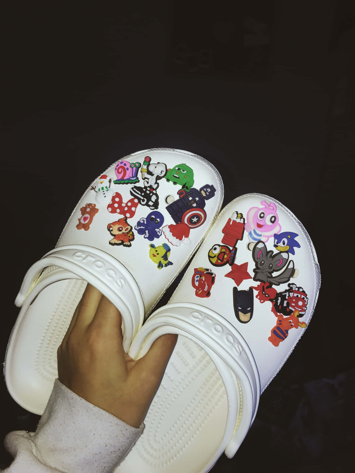 白色Crocs涼鞋裝飾住卡通同超級英雄貼紙，由一隻手拎住。