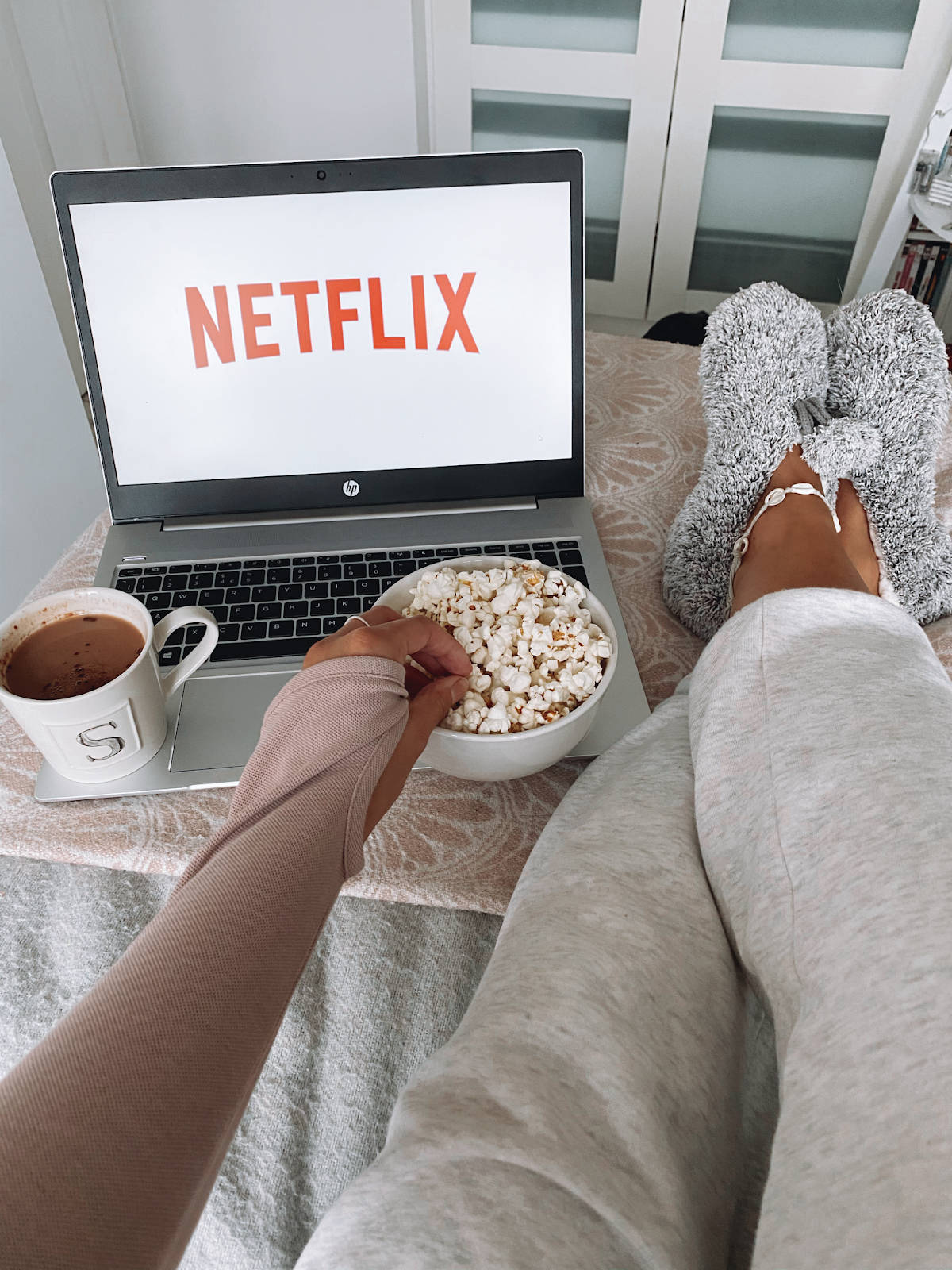 Netflix 桌布 壁紙 — 舒適的人穿著毛絨襪子吃爆米花，同時在筆記型電腦上觀看Netflix，附近有熱巧克力。