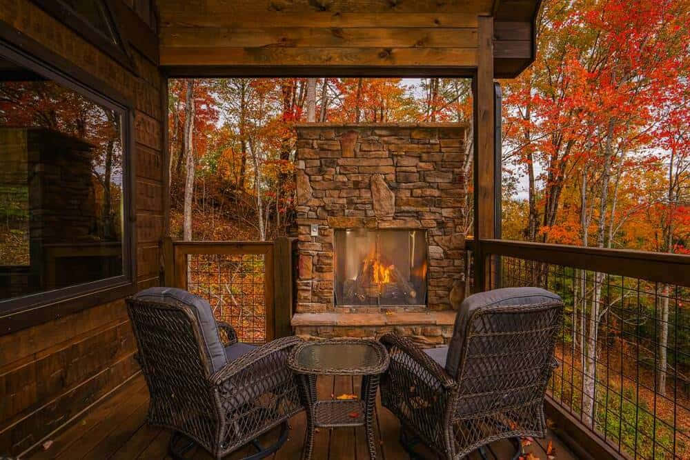 Fall Cabin 桌布 壁紙 — 舒適的柳條椅圍繞著石壁爐，位於木製甲板上，俯瞰充滿活力的秋日森林。