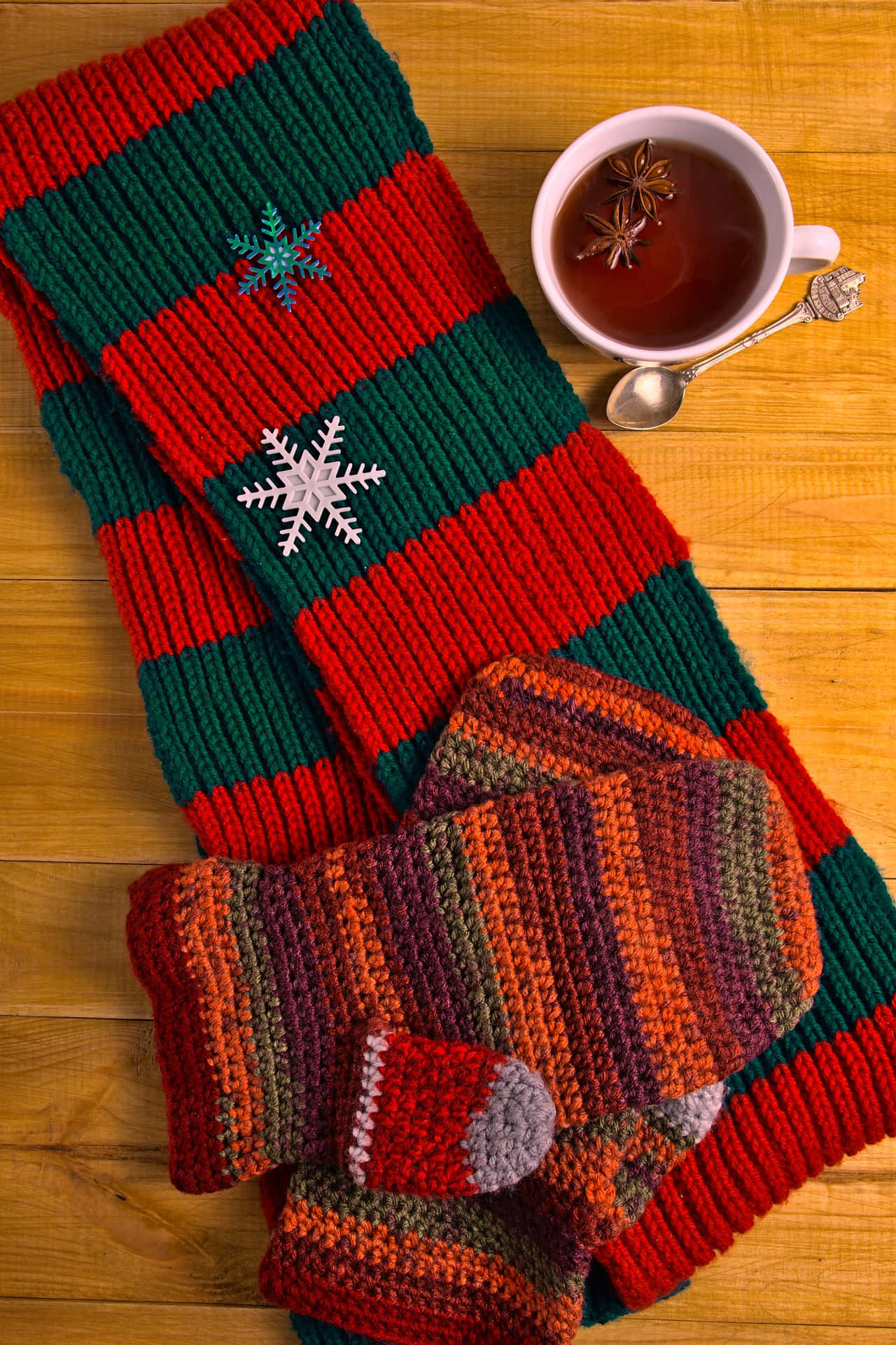 Mittens 桌布 壁紙 — 舒適的紅綠針織圍巾和手套，帶有雪花裝飾，放在木桌上的一杯香料茶旁邊。