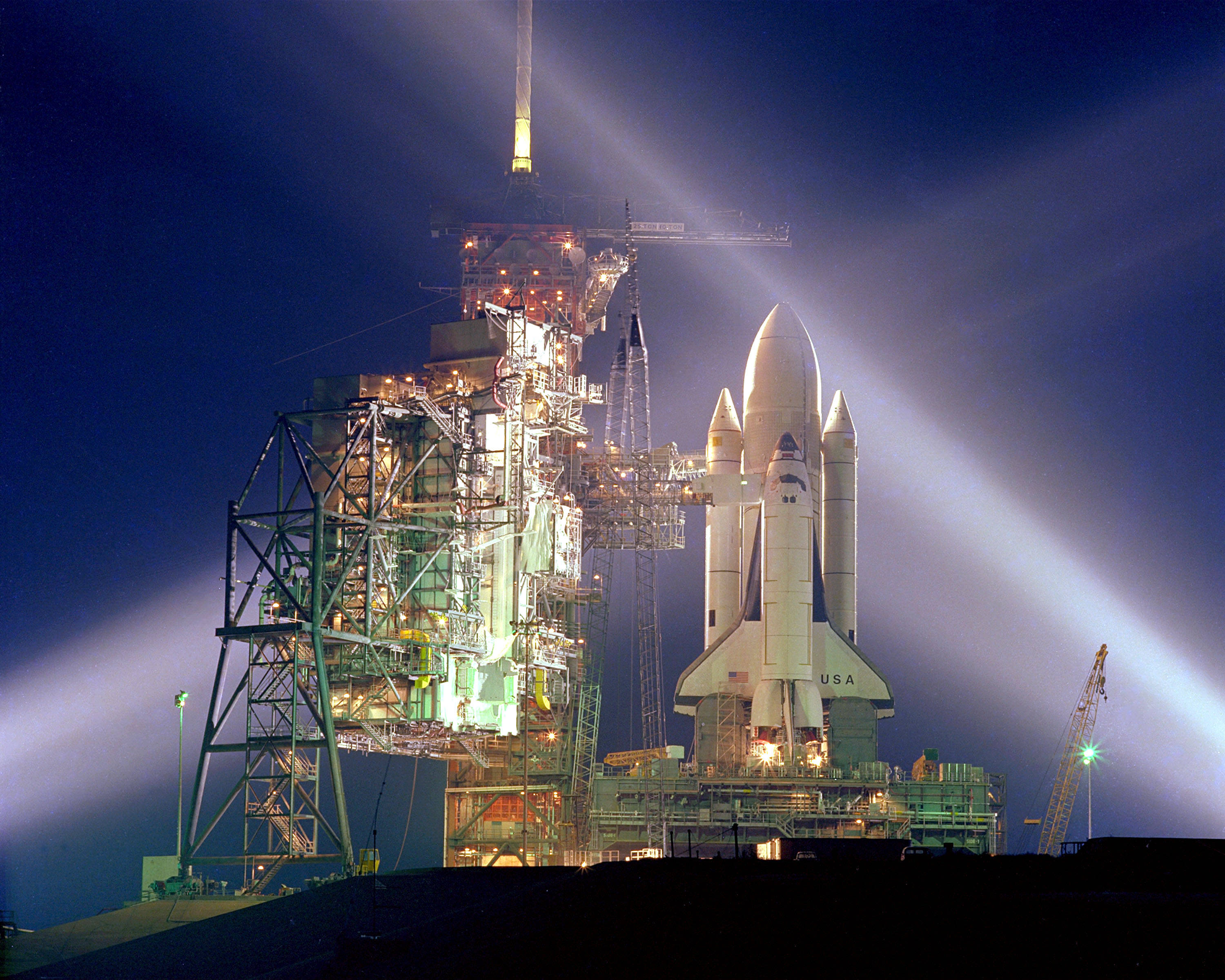 航空航天 STS-1 太空飛行 壁紙 — 一架美國太空總署的太空穿梭機在夜間矗立在發射台上，明亮的聚光燈劃破漆黑的天空。