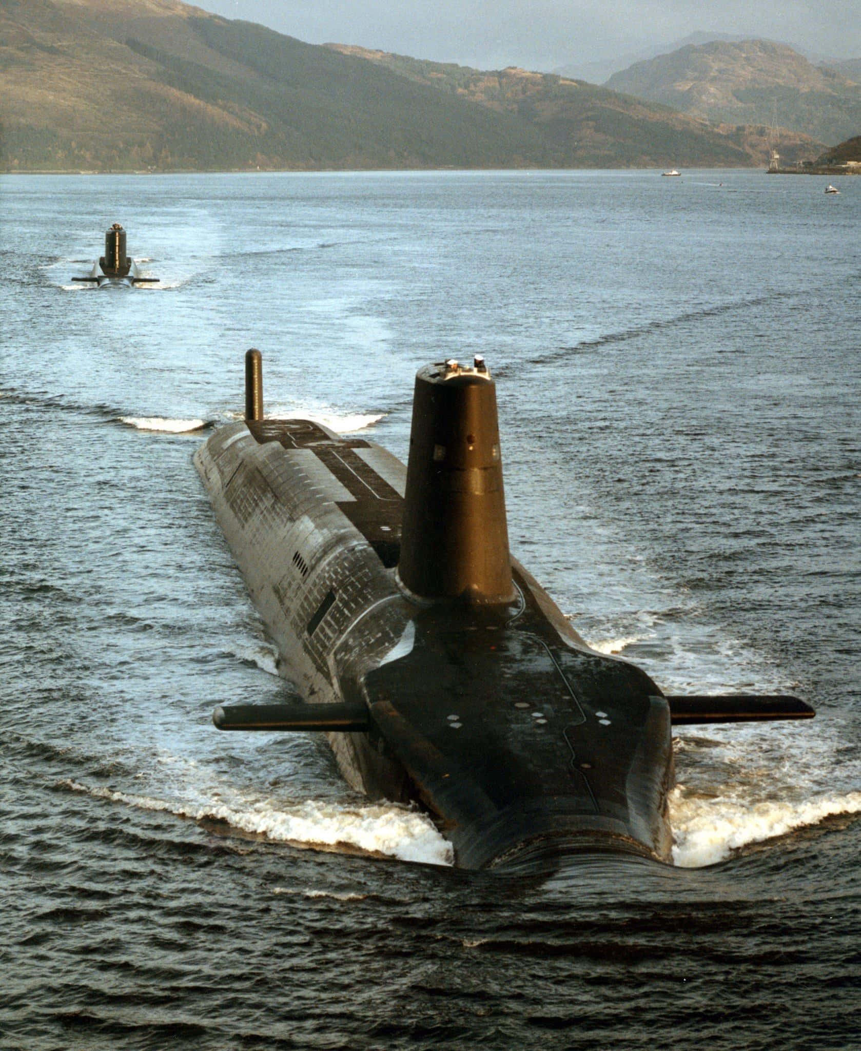 艦長潛艇駛向深海 壁紙 — 兩艘流線型的黑色潛艇在平靜的水域中滑行，遠處朦朧的山巒聳立。