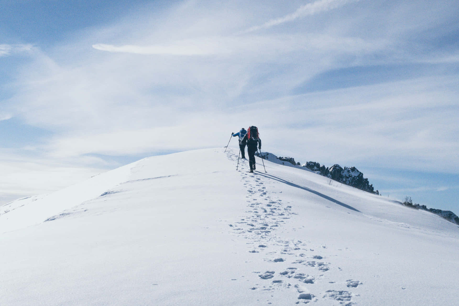 兩名遠足者正在攀登積雪的山脊，雪地上清晰可見腳印。