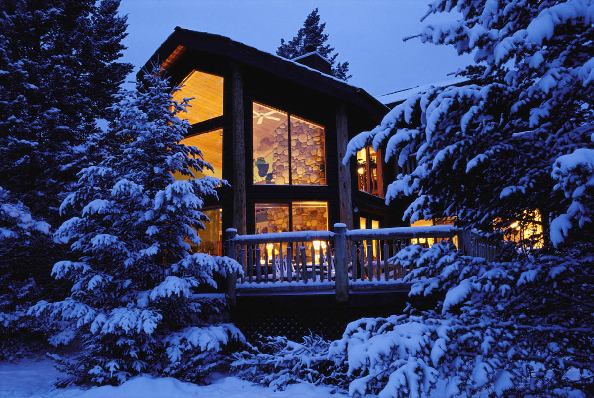 色彩對比冬日小屋 壁紙 — 一間舒適的木屋坐落在白雪覆蓋的松樹之間，在暮色天空的映襯下從內部散發出溫暖的光芒。