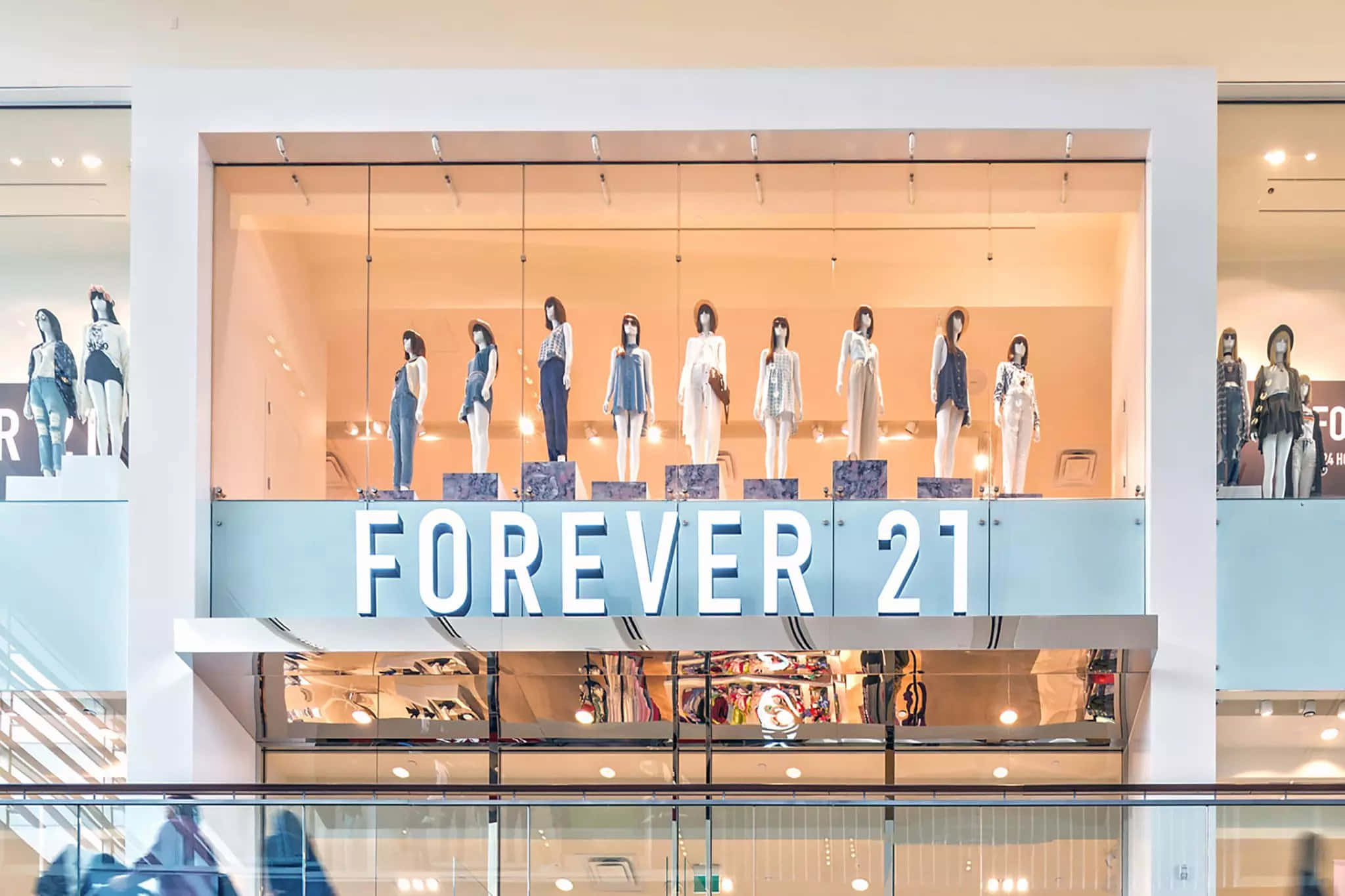 色彩繽紛、時尚有型，與Forever 21一起活出精彩人生 壁紙 — Forever 21 店舖櫥窗展示，燈光明亮，人體模型穿著時尚服飾，背景為溫暖的蜜桃色。