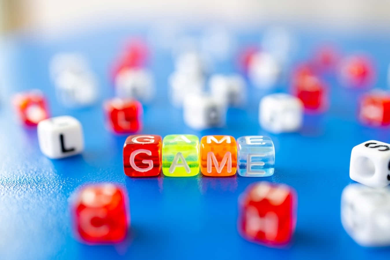 game 桌布 壁紙 — 色彩繽紛嘅字母骰子喺充滿活力嘅藍色表面上拼出GAME，周圍散落紅色同白色骰子，呈現柔和焦點。