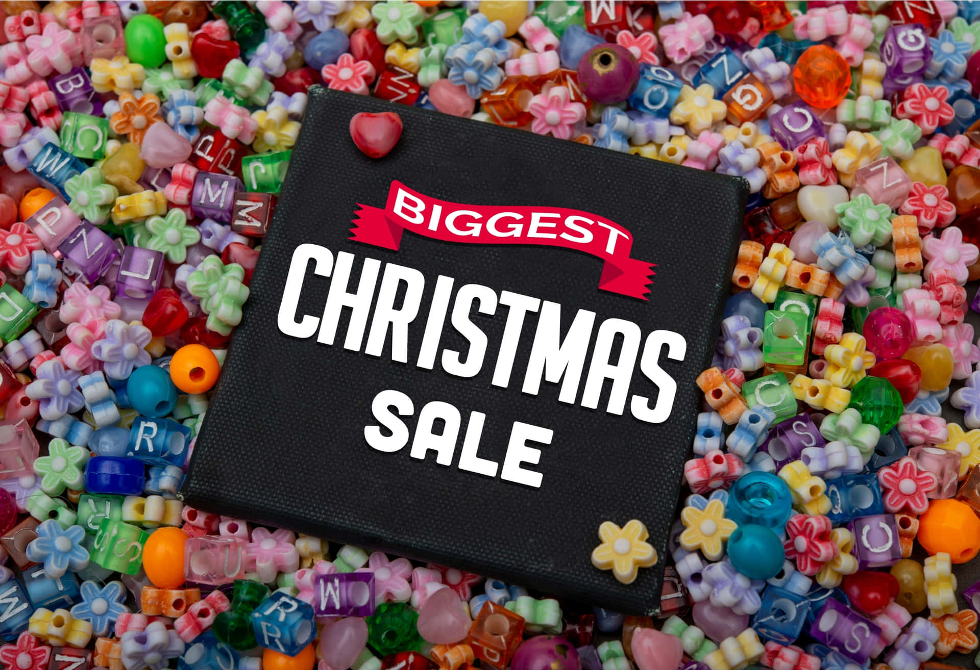 黑色標牌，寫有「Biggest Christmas Sale」，周圍環繞著色彩繽紛的字母和花朵珠子。