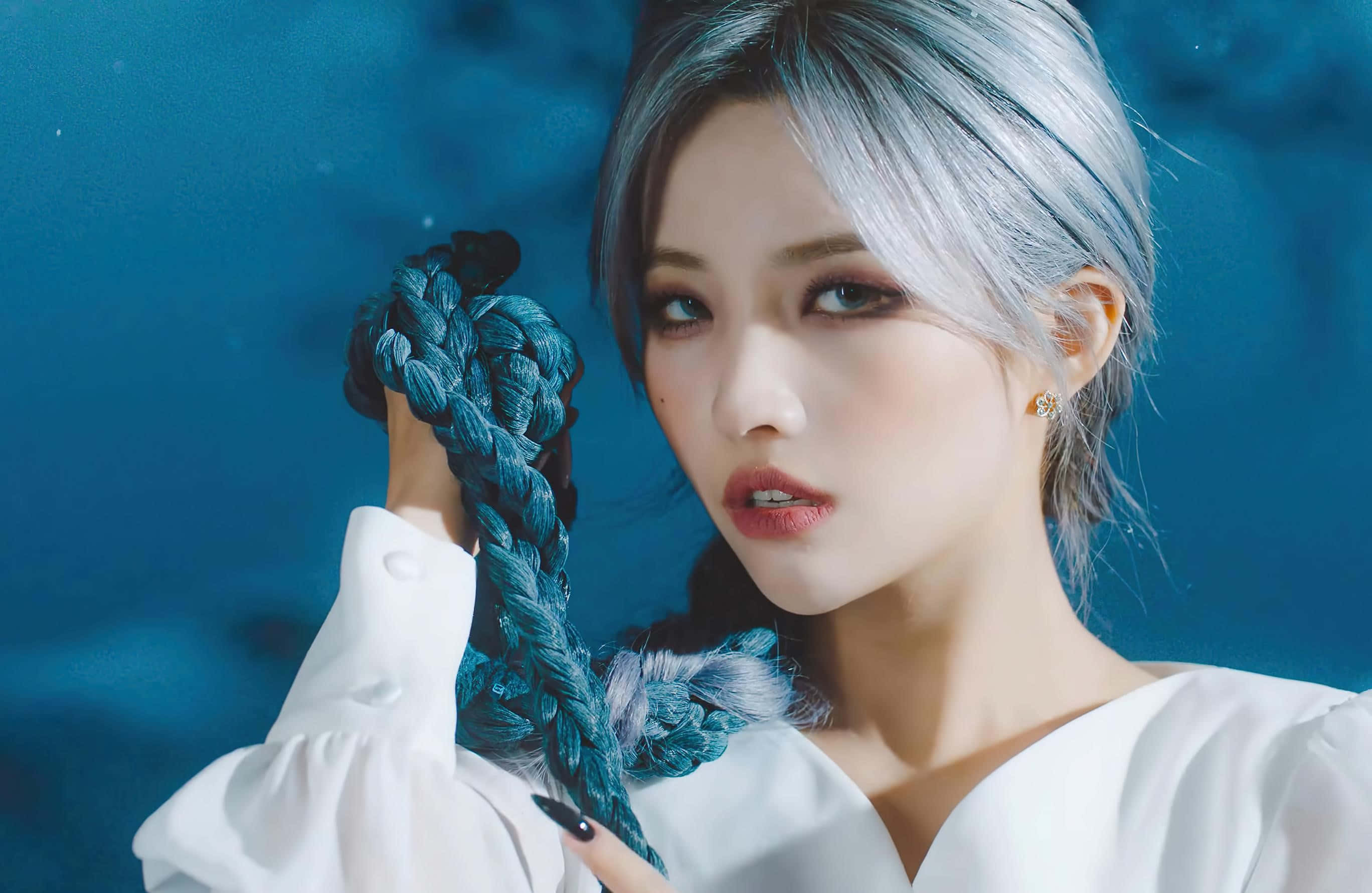 色彩繽紛的 K-pop 組合舞台表演 壁紙 — 一位銀髮女性在深藍色背景前拿著一條青綠色的編織繩。