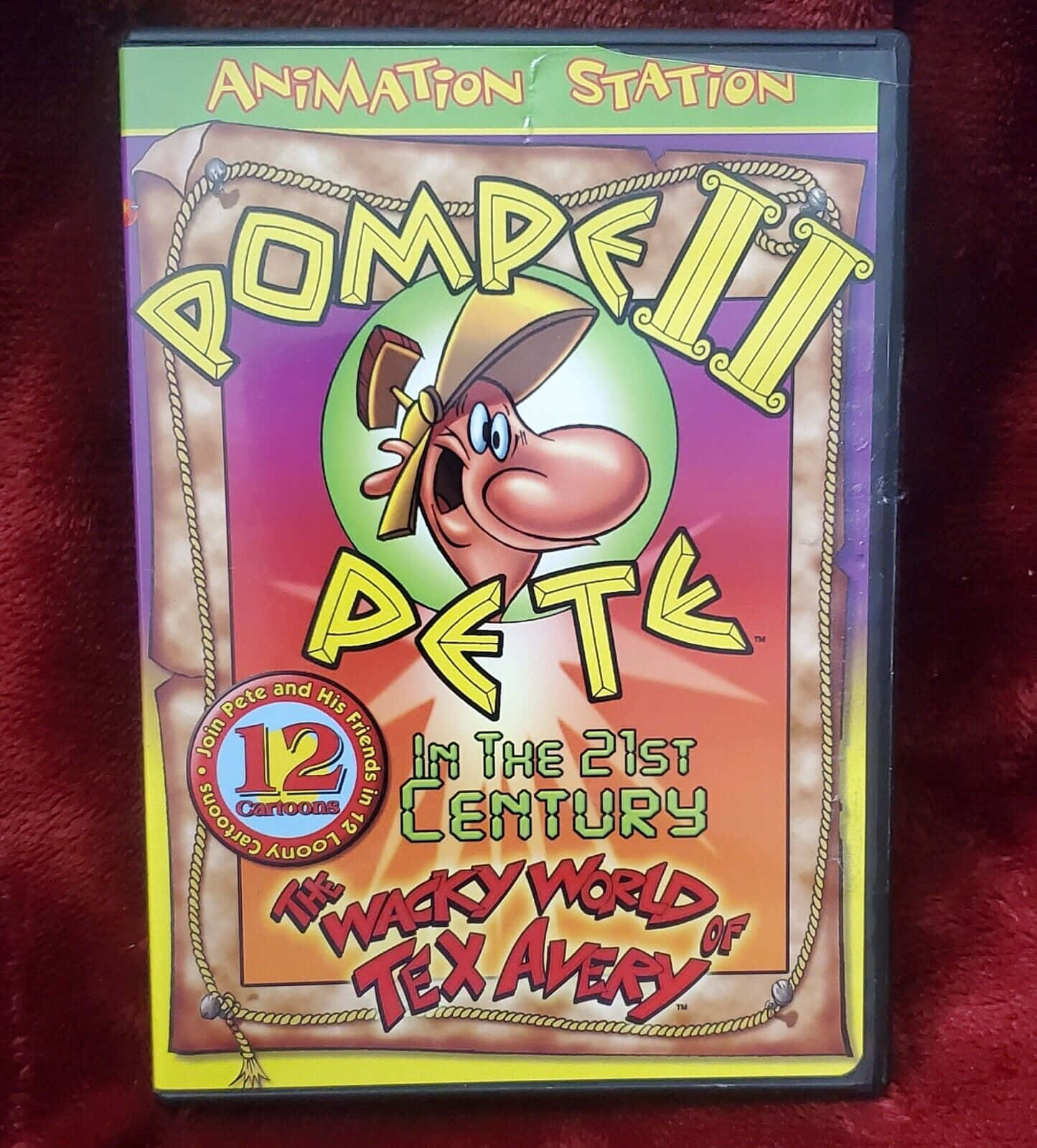 The Wacky World Of Tex Avery 桌布 壁紙 — 色彩繽紛的DVD封面，用於「龐貝皮特」卡通系列，放置在柔軟的紅色天鵝絨表面上。