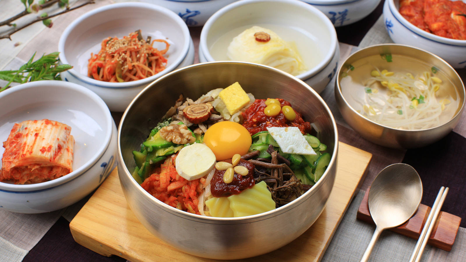 色彩繽紛的傳統韓國料理——拌飯 壁紙 — 一碗色彩繽紛的韓國石鍋拌飯，上面放有生雞蛋和各種蔬菜，周圍伴以小菜，置於木托盤上。