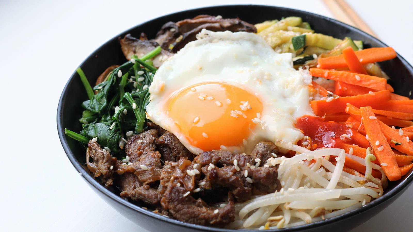 色彩繽紛的傳統韓式拌飯 壁紙 — 一碗色彩繽紛的韓國石鍋拌飯，上面放著太陽蛋、芝麻和五顏六色的蔬菜。
