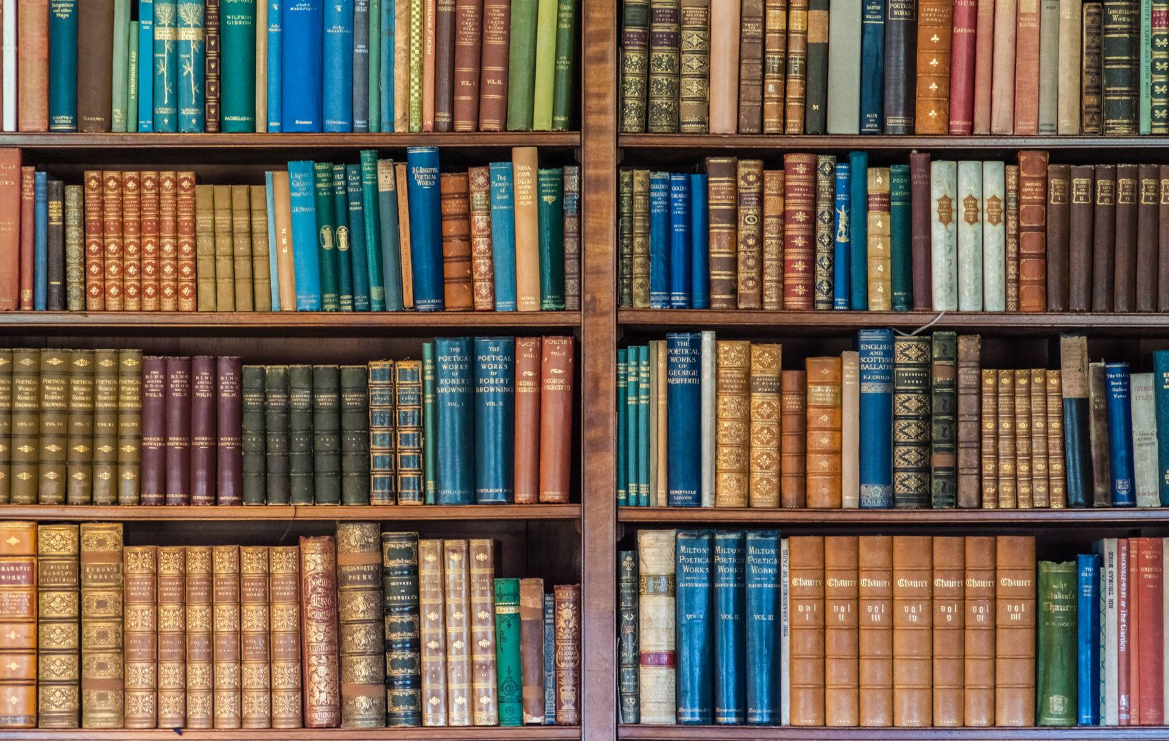 色彩繽紛的古董書籍書架 壁紙 — 高大的木製書架上擺滿了排列整齊的復古書籍，色調豐富，包括藍色、棕色和金色。