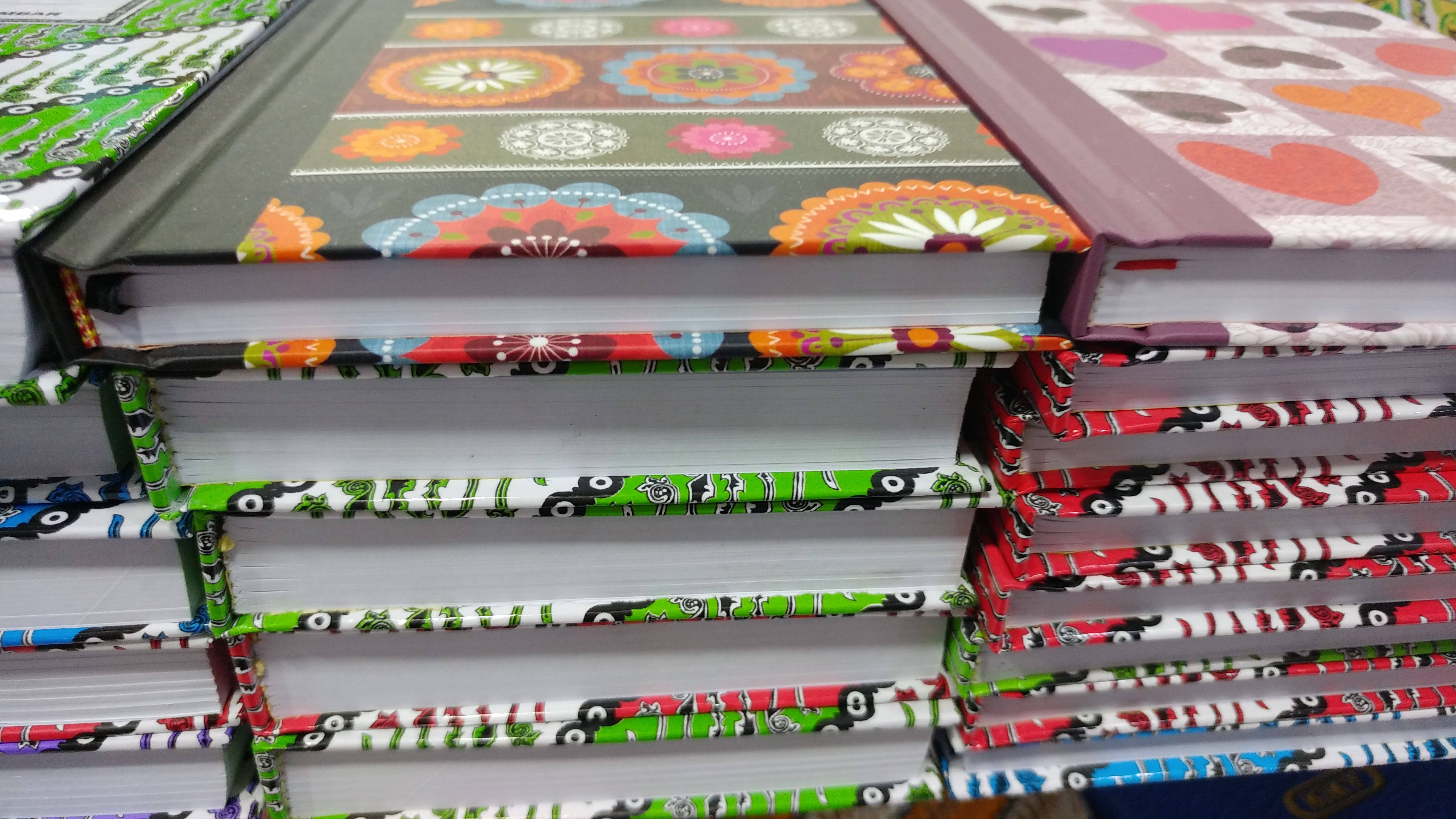 書籍 桌布 壁紙 — 色彩繽紛的圖案書籍堆疊，帶有鮮豔的花卉和幾何封面，以特寫視角排列。