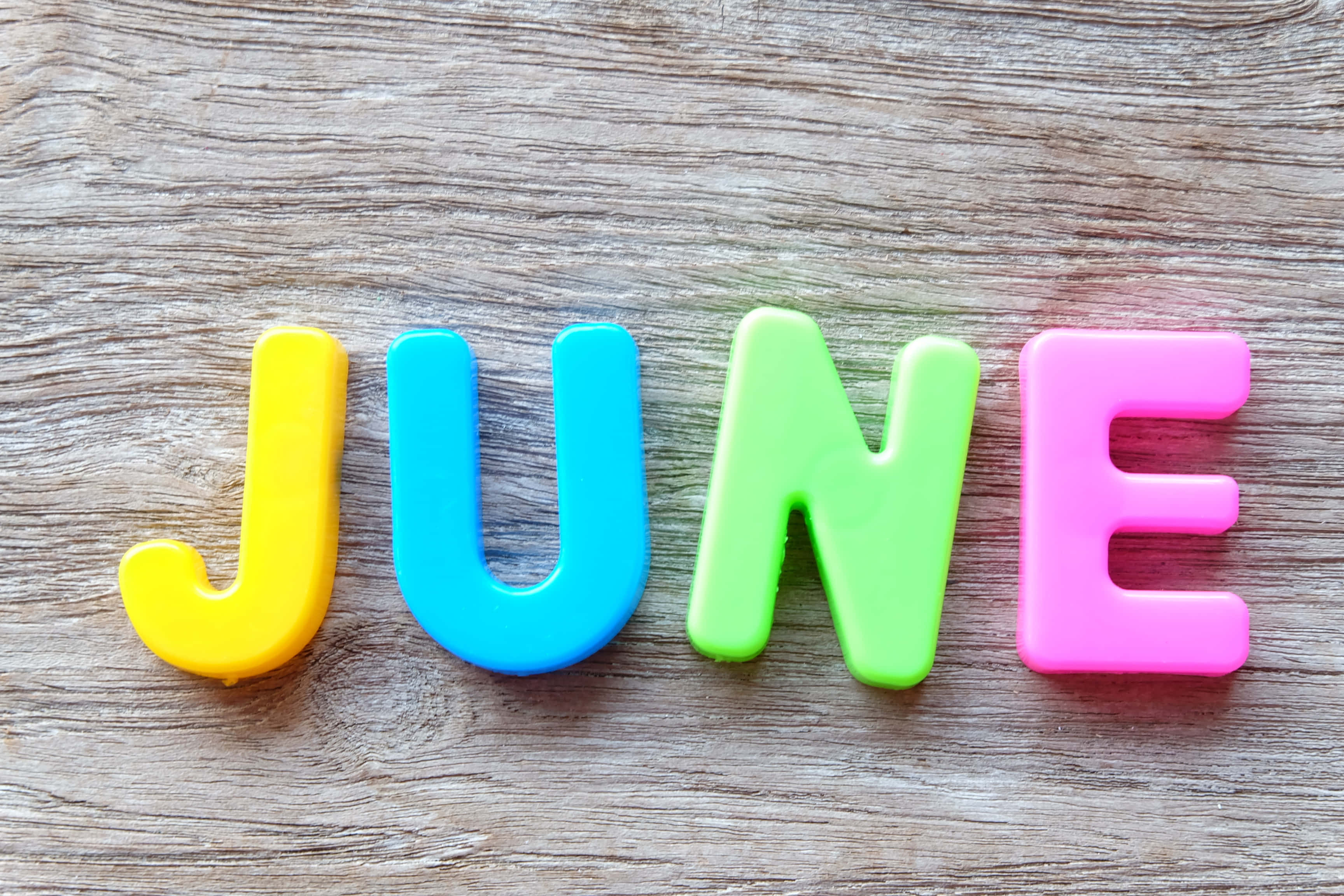 June 桌布 壁紙 — 色彩繽紛的塑膠字母拼出 JUNE，排列在帶有紋理的木質表面上。