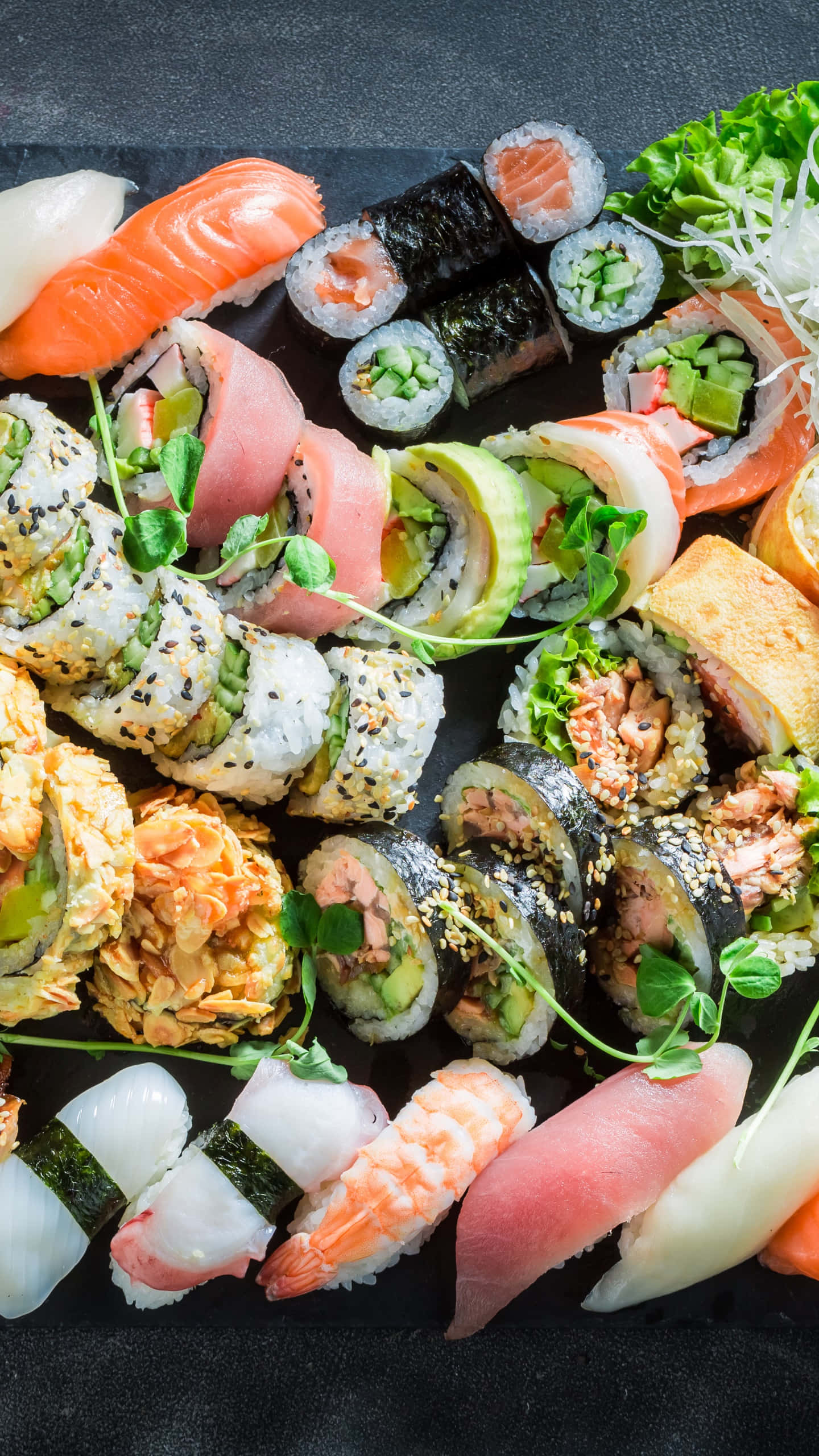 Sushi 桌布 壁紙 — 色彩繽紛的壽司卷和握壽司拼盤，藝術性地擺放在深色石板盤上，以微型蔬菜裝飾。