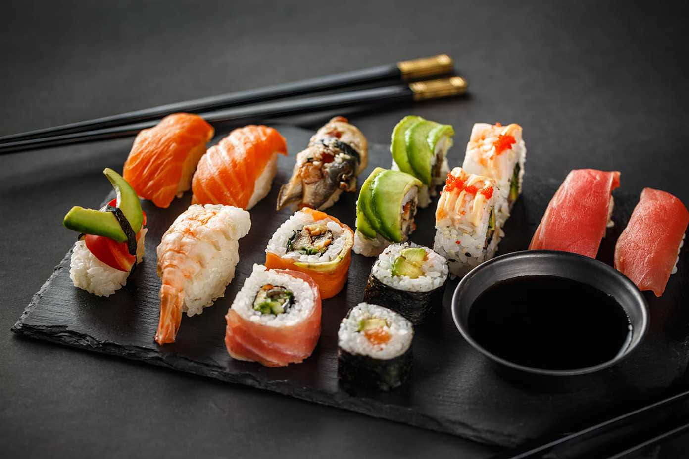 Sushi 桌布 壁紙 — 色彩繽紛的壽司拼盤，藝術性地擺放在深色石板碟上，配以醬油和筷子，令人垂涎。