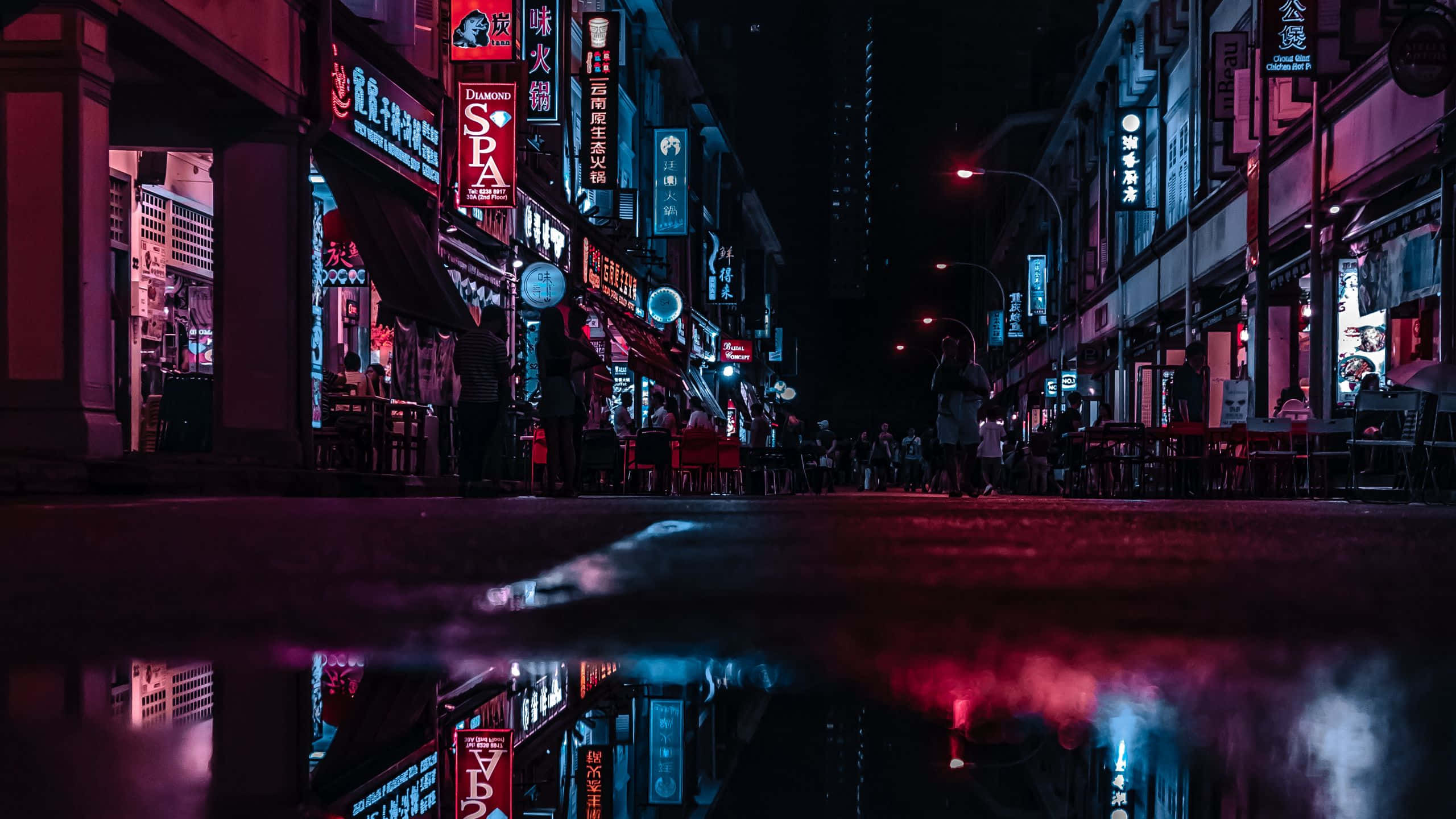 色彩繽紛的山谷美景 壁紙 — 一條霓虹燈照亮的城市街道在夜晚倒映在雨水坑中，帶有發光的招牌和剪影般的行人。
