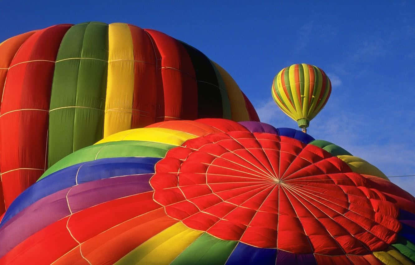 Balloon 桌布 壁紙 — 色彩繽紛的彩虹熱氣球以鮮豔色彩和幾何圖案點綴清澈的藍天。