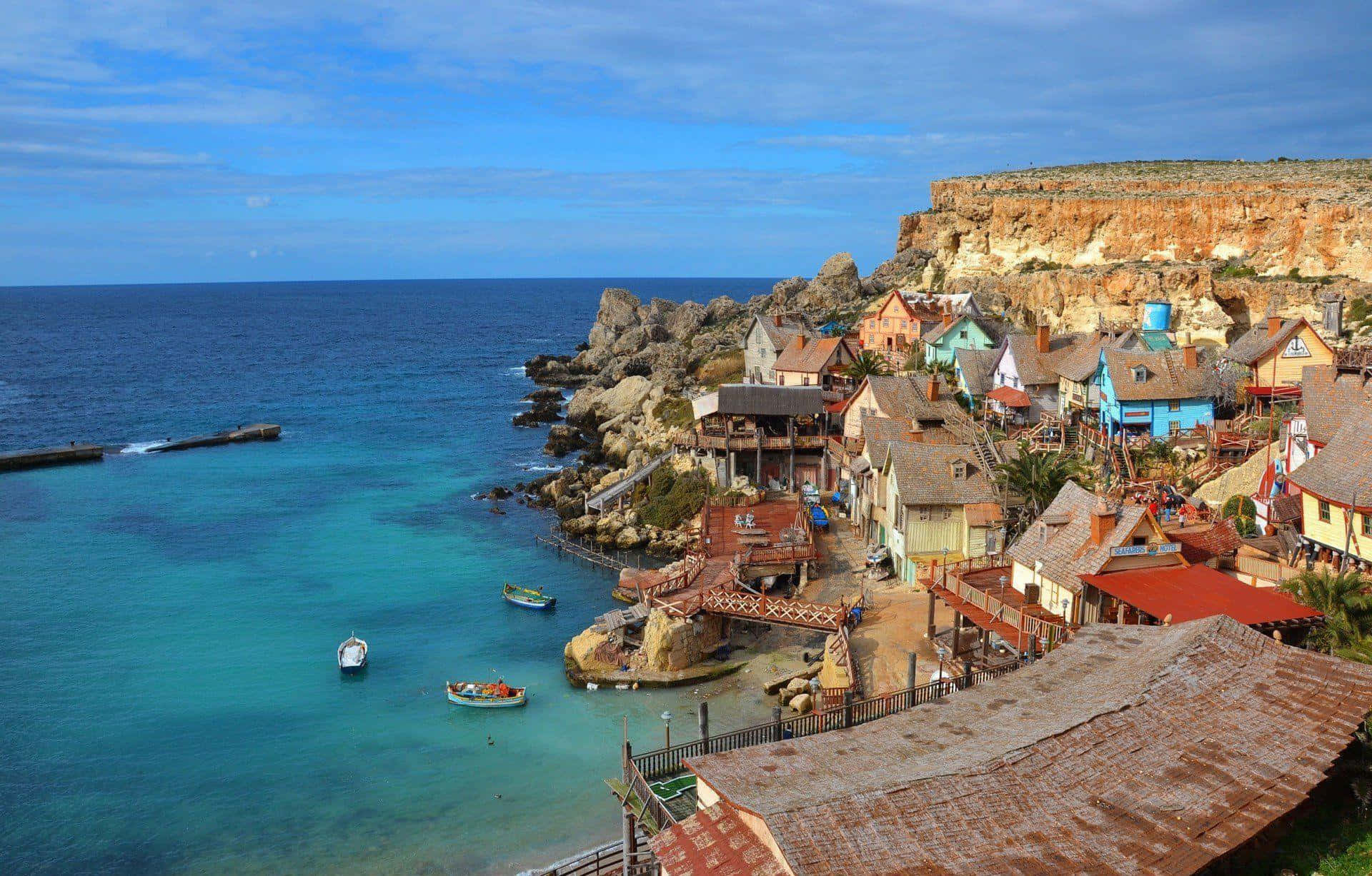 Malta 桌布 壁紙 — 色彩繽紛的懸崖村莊，質樸的房屋坐落在碧綠海水之上，小船漂浮在岩石海岸附近。