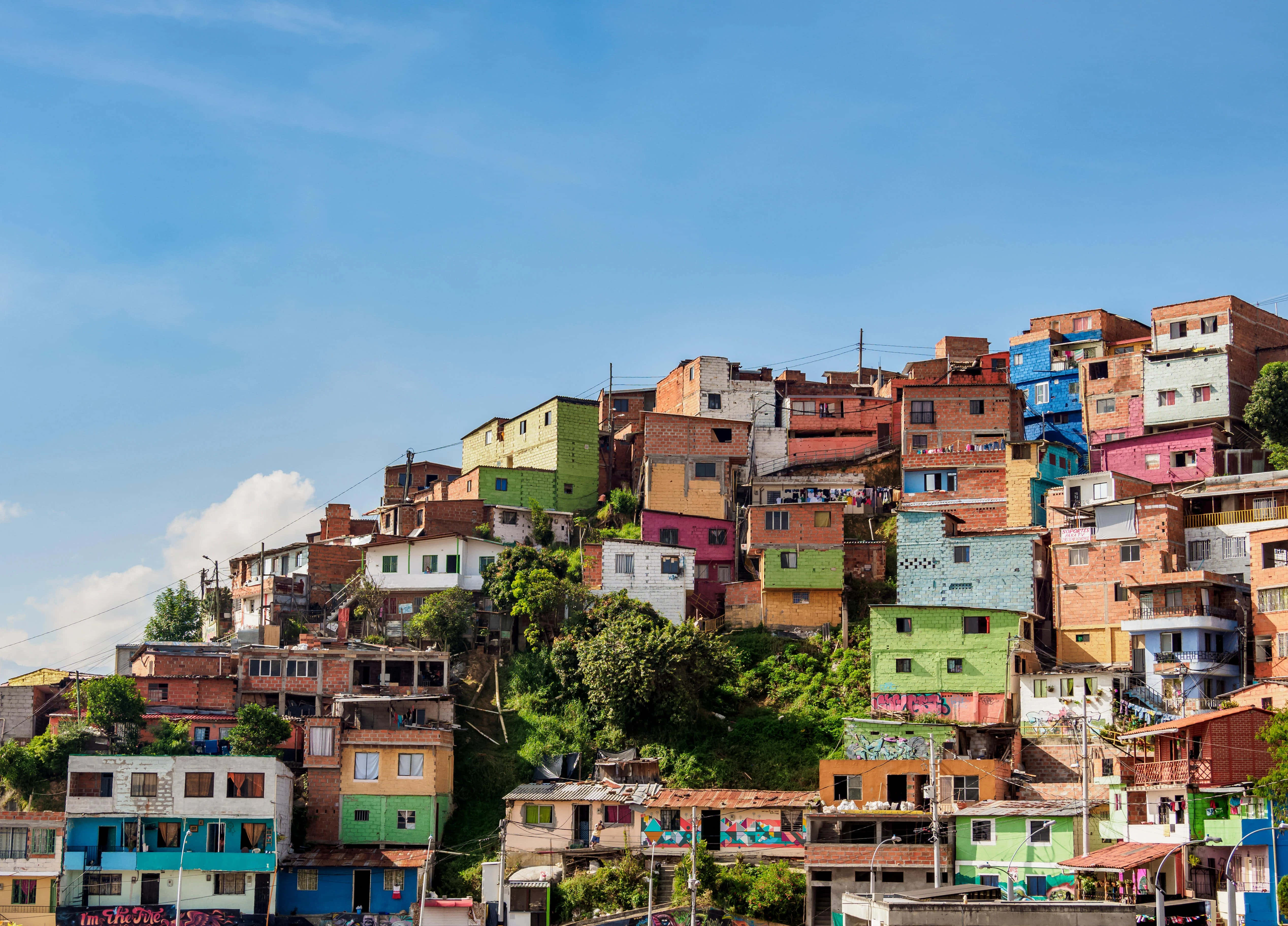 Colombia 桌布 壁紙 — 色彩繽紛的房屋在晴朗藍天和零星白雲下，沿著陽光普照的山坡層層疊疊。