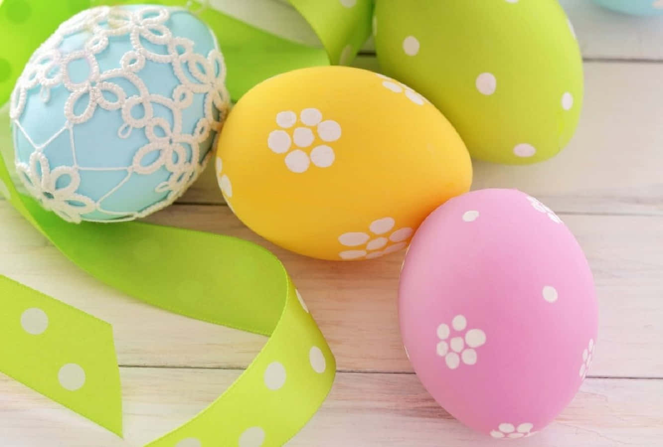 Pastel Easter 桌布 壁紙 — 色彩繽紛的手工裝飾復活節蛋，帶有蕾絲和花卉圖案，放在一條亮綠色絲帶上，置於淺色木質表面。