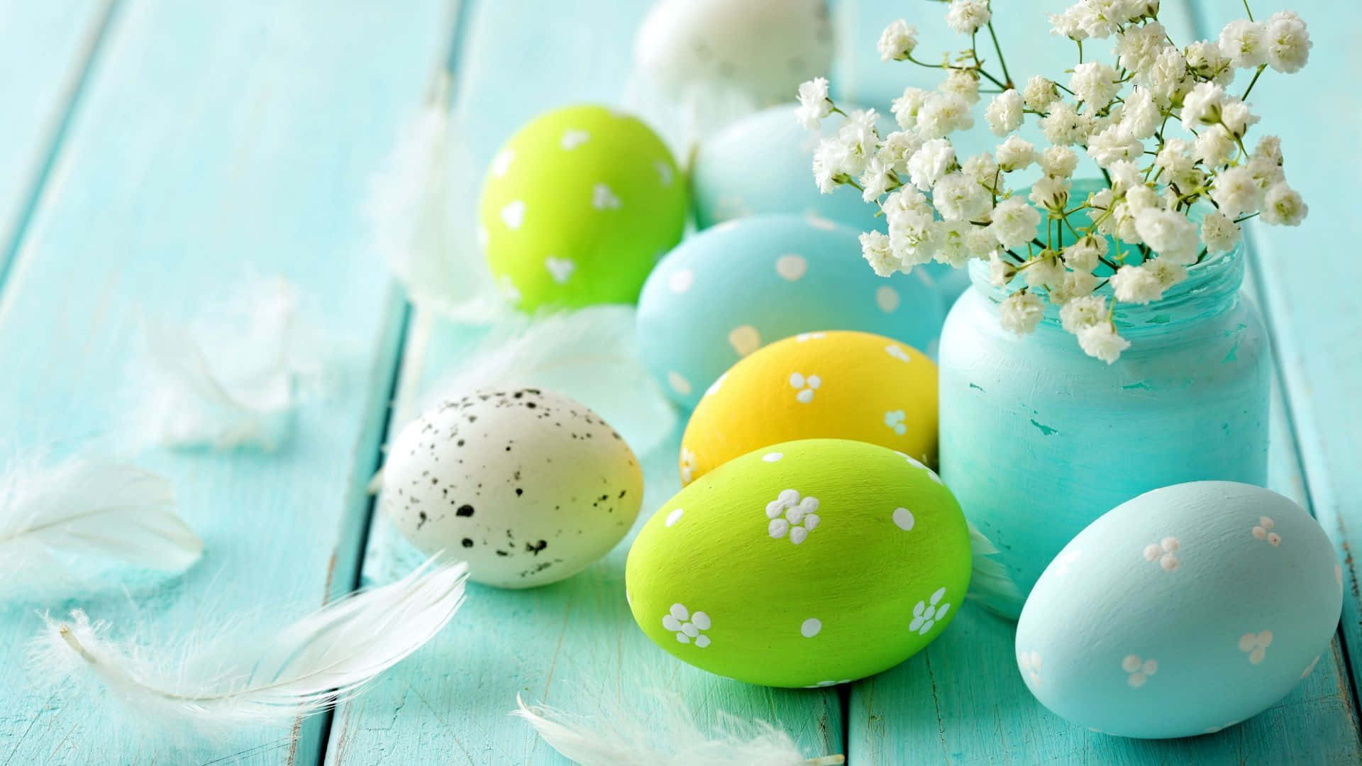 Spring Pastel 桌布 壁紙 — 色彩繽紛的手繪復活節彩蛋，帶有花卉圖案和白色羽毛，放置在風化的藍綠色木質表面上，旁邊放著一瓶滿天星。
