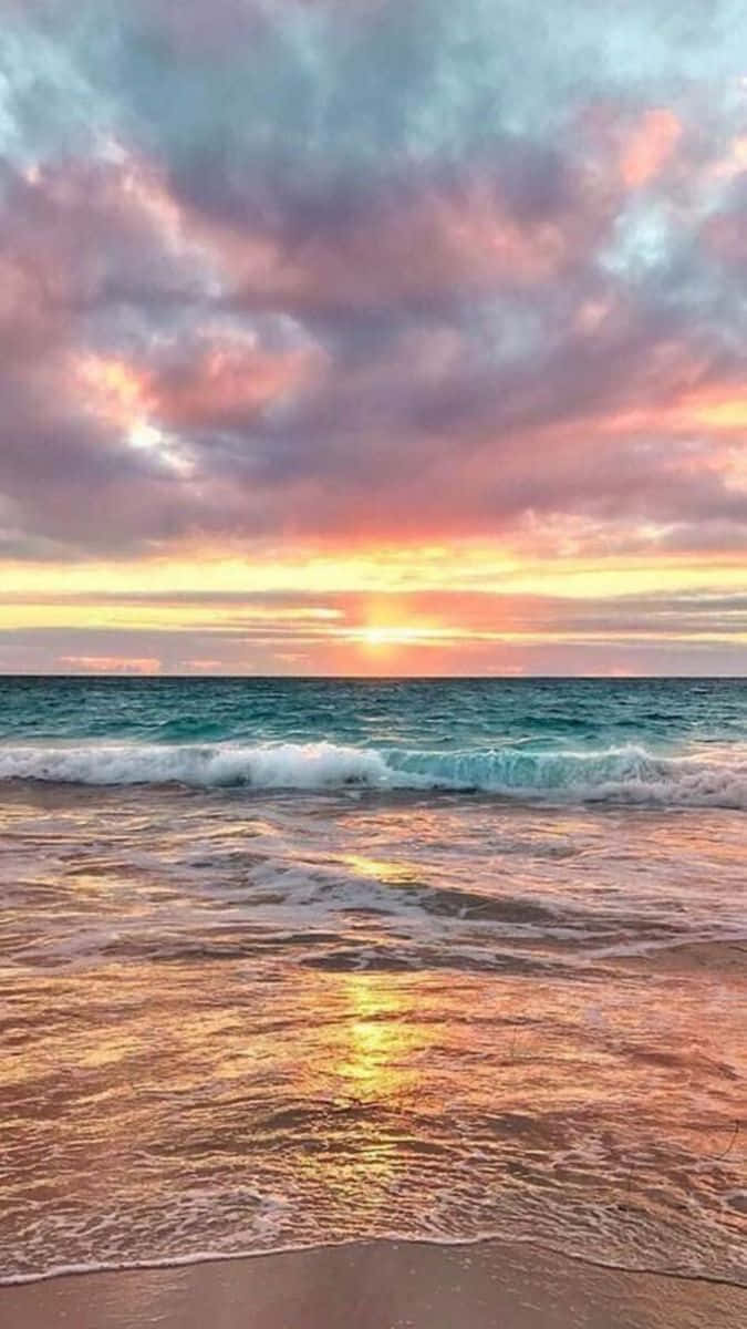 色彩繽紛的日落海灘圖 壁紙 — 夕陽將天空染成粉紅、橙色和紫色，海浪拍打沙灘，反射出金色的光芒。