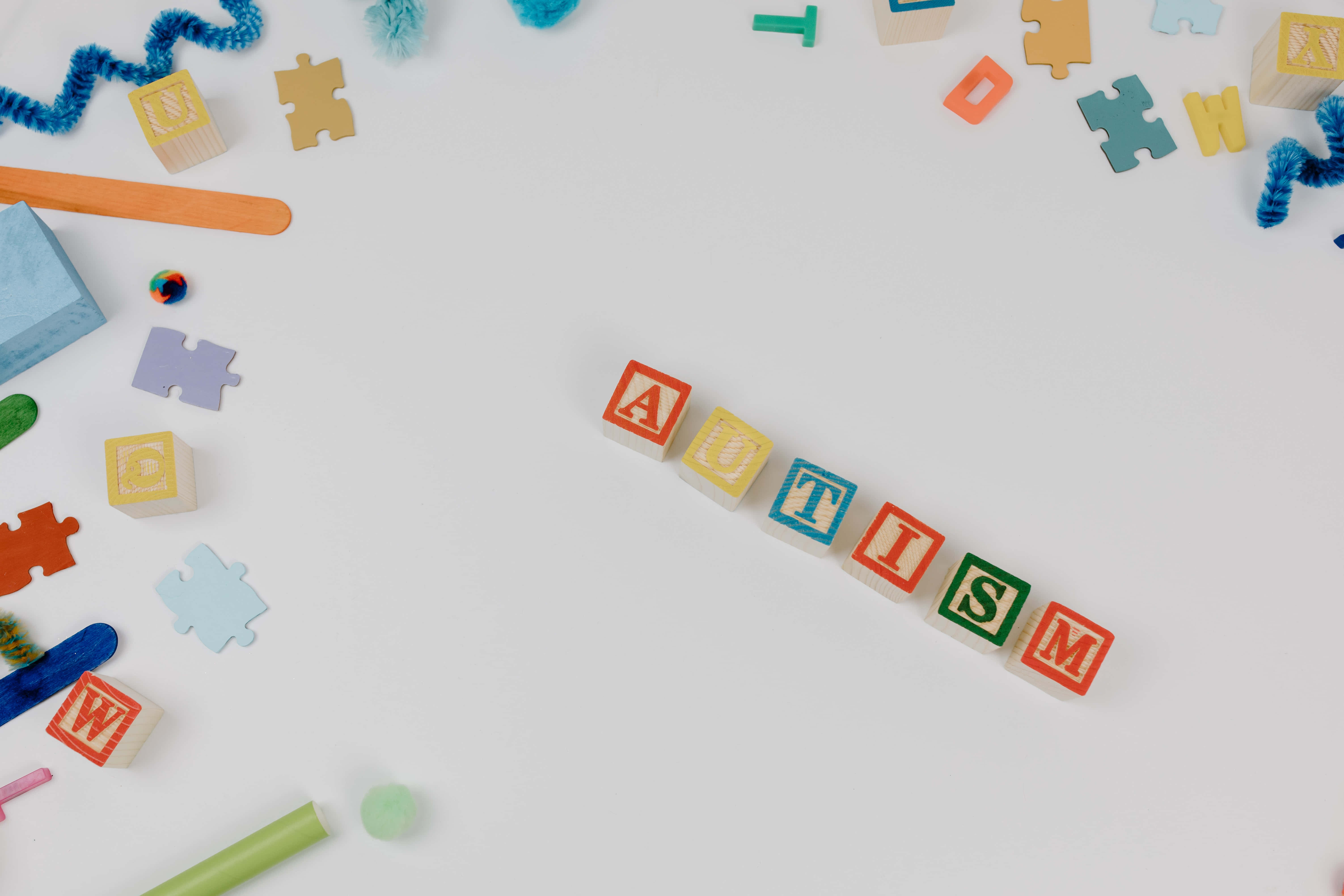 Autism 桌布 壁紙 — 色彩繽紛的木製積木拼出「自閉症」字樣，周圍環繞著拼圖碎片和手工藝用品，置於白色表面上。