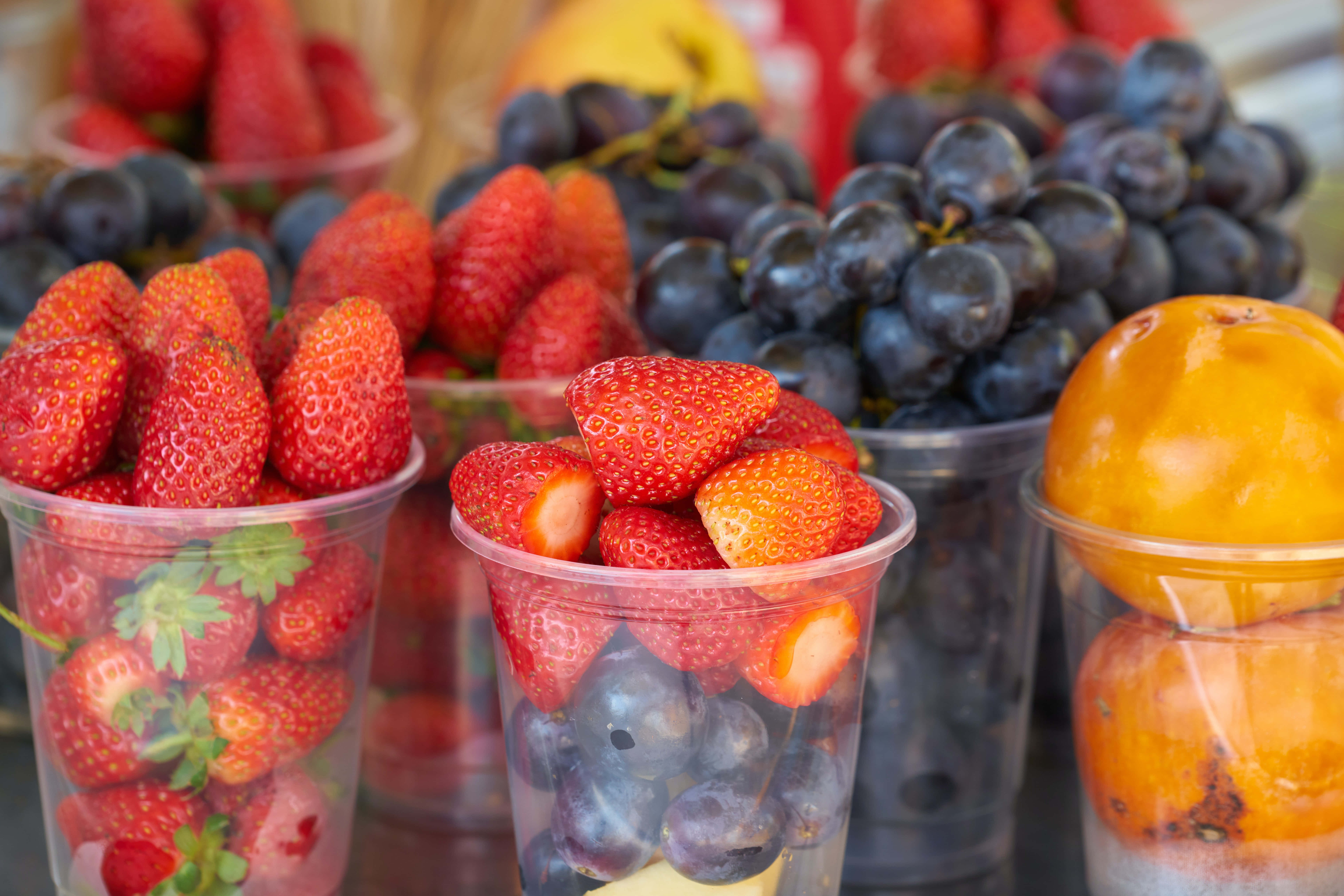 Summer Fruits 桌布 壁紙 — 色彩繽紛的杯子盛滿新鮮草莓、葡萄和柿子，營造出色彩豐富的水果市場展示。