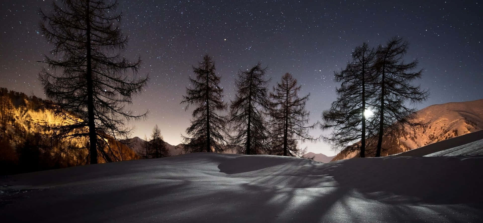 夜晚被雪覆蓋的山脈，明亮的月亮下樹木和星星。