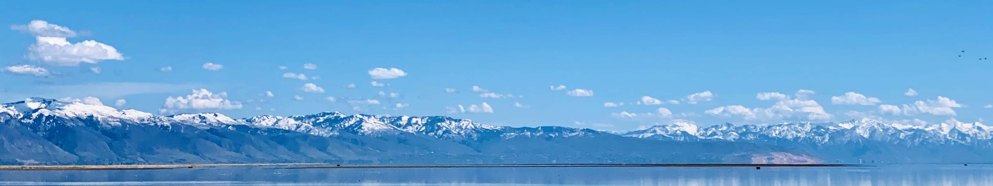 色彩繽紛的機場場景 壁紙 — 廣闊平靜的湖面映照著白雪覆蓋的山脈，天空湛藍，白雲點綴。