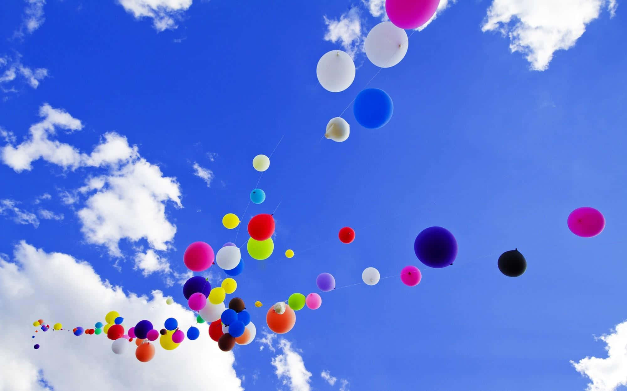 Balloon 桌布 壁紙 — 色彩繽紛的氣球如瀑布般向上飄浮，背景是點綴著蓬鬆白雲的明亮藍天。