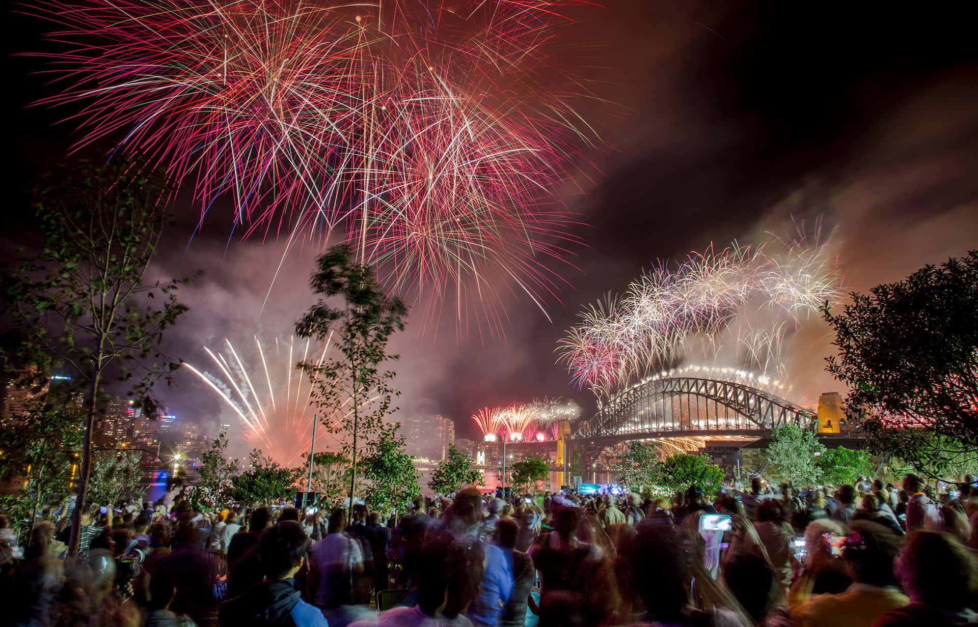 New Years Eve 桌布 壁紙 — 色彩繽紛的煙花在悉尼海港大橋上空綻放，人群在漆黑的夜空下敬畏地觀看。