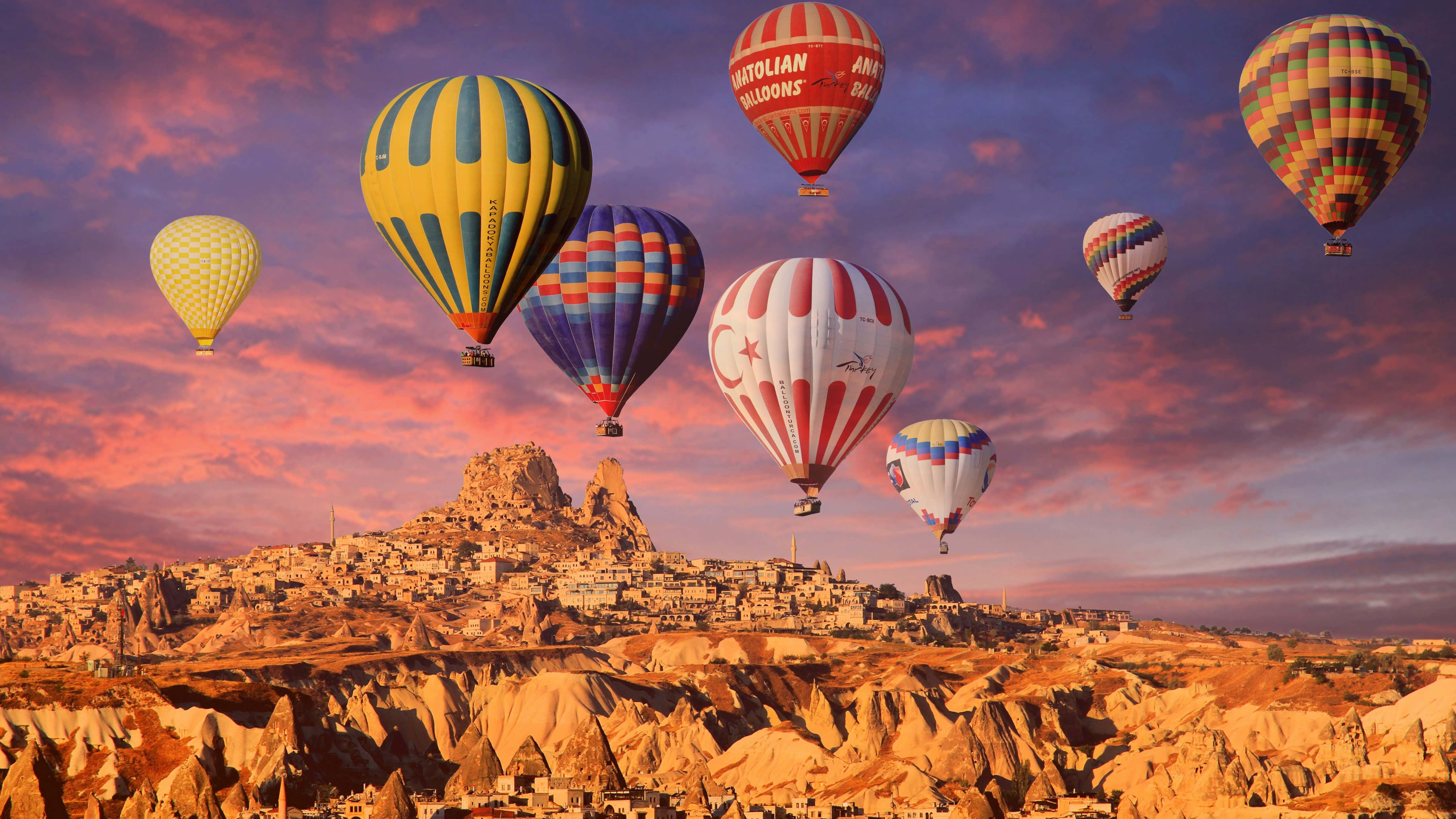 Hot Air Balloon 桌布 壁紙 — 色彩繽紛的熱氣球在日落時分飄過崎嶇的山谷，位於歷史悠久的懸崖小鎮之上。