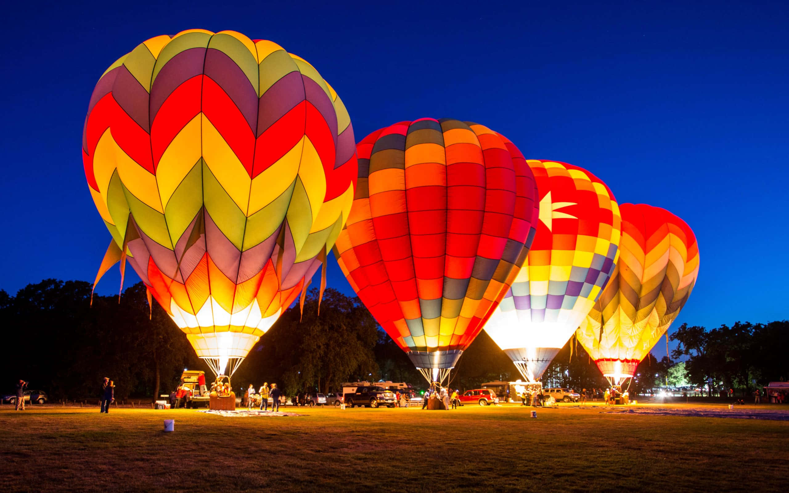 熱氣球 桌布 壁紙 — 色彩繽紛的熱氣球在深藍色暮色天空下，於草地上散發溫暖的光芒。