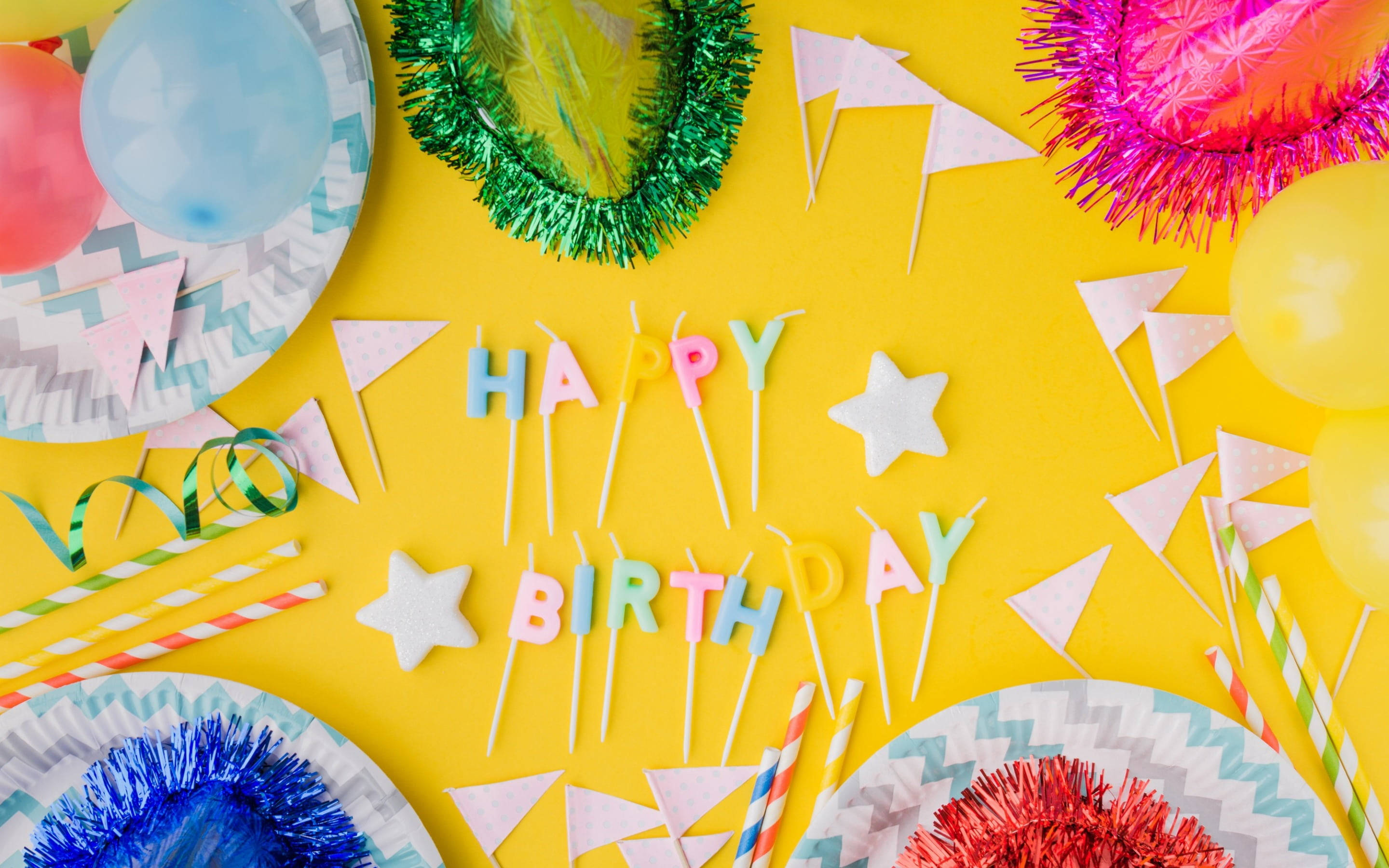 Birthday Party 桌布 壁紙 — 色彩繽紛的生日派對用品擺放在明亮的黃色背景上，配有彩色氣球和節日裝飾。