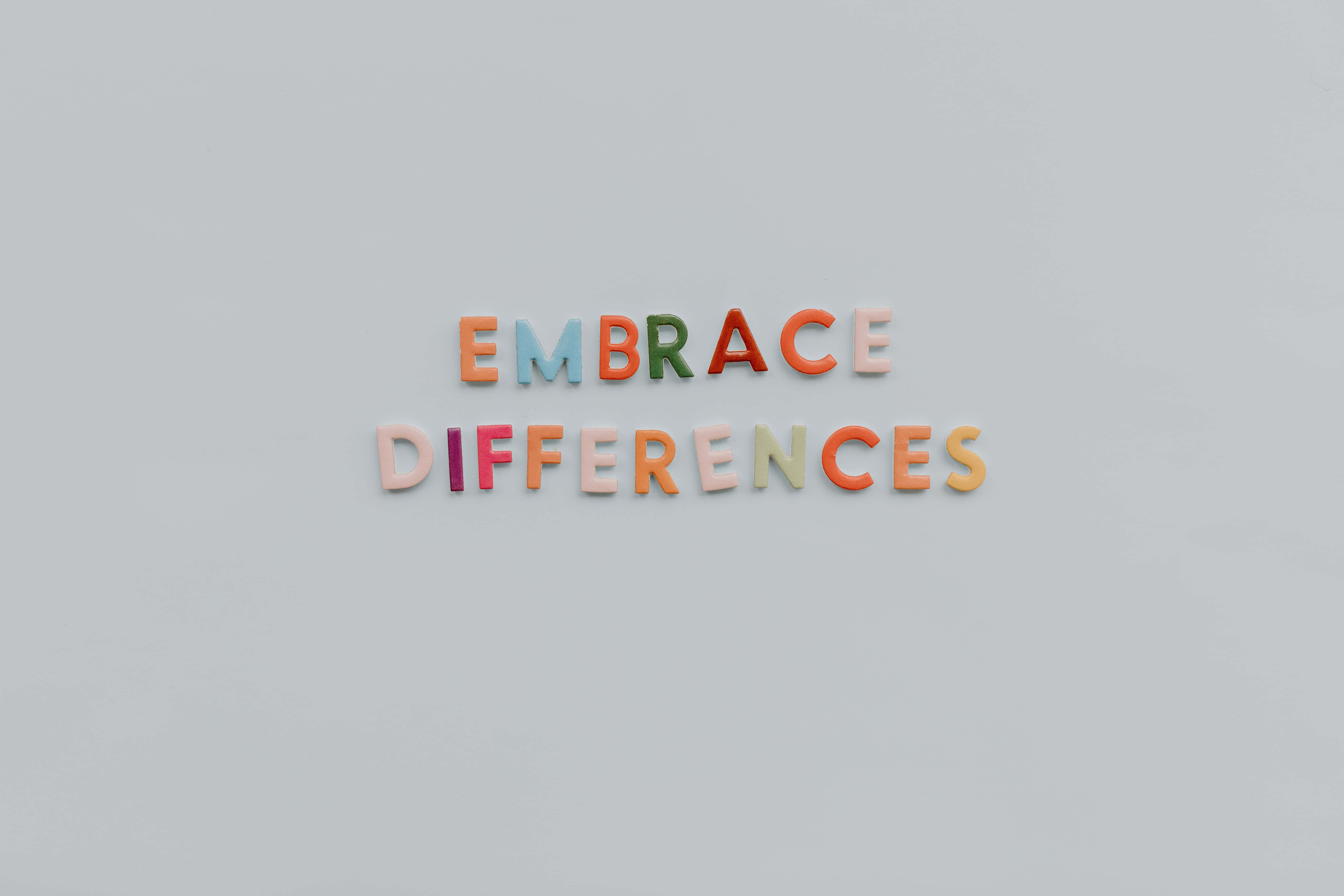 Autism 桌布 壁紙 — 色彩繽紛的磁石字母在純灰色表面上拼出「EMBRACE DIFFERENCES」。