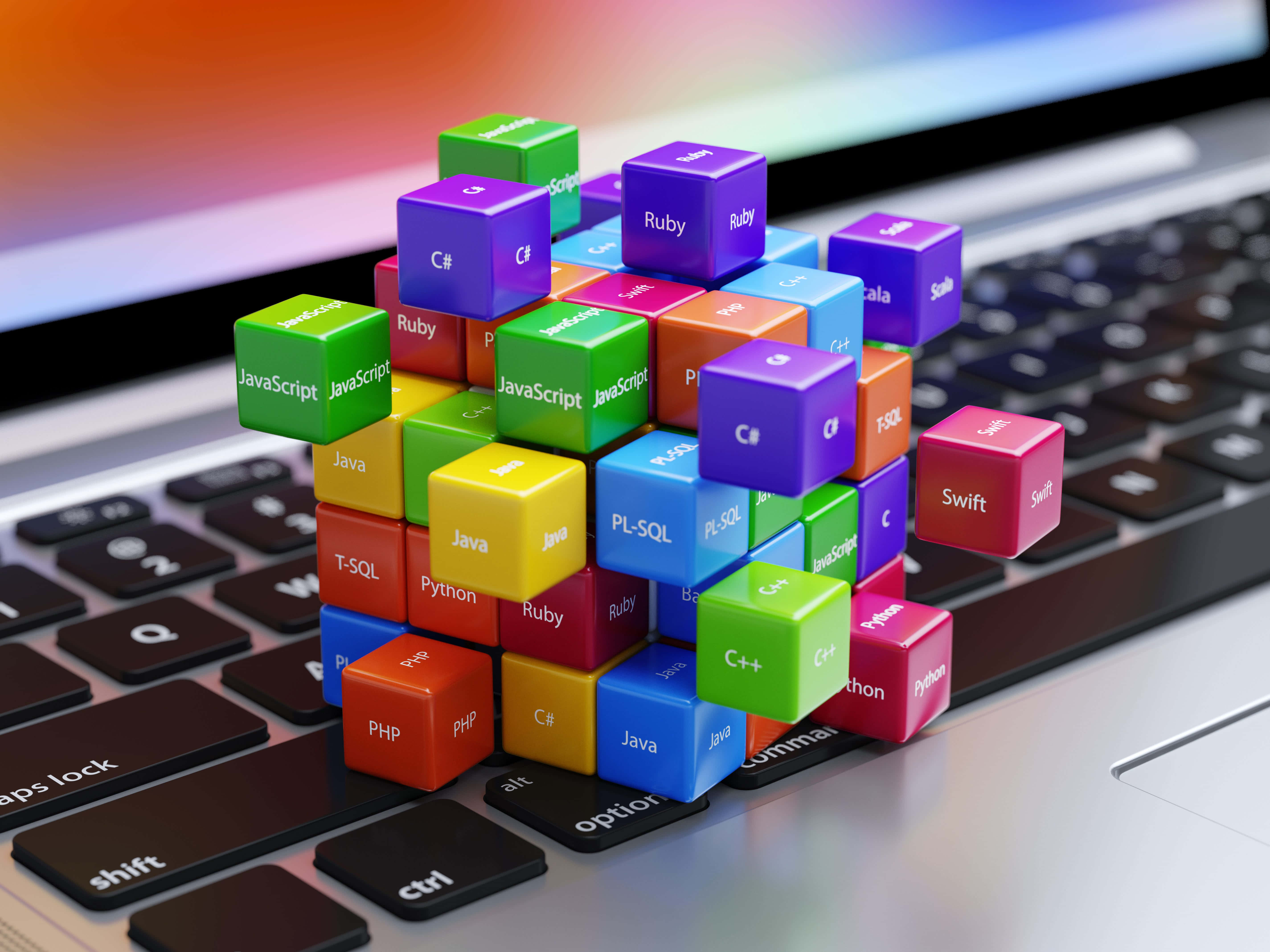 Programming 桌布 壁紙 — 色彩繽紛的立方體標有程式語言，漂浮在數位工作空間的筆記型電腦鍵盤上方。