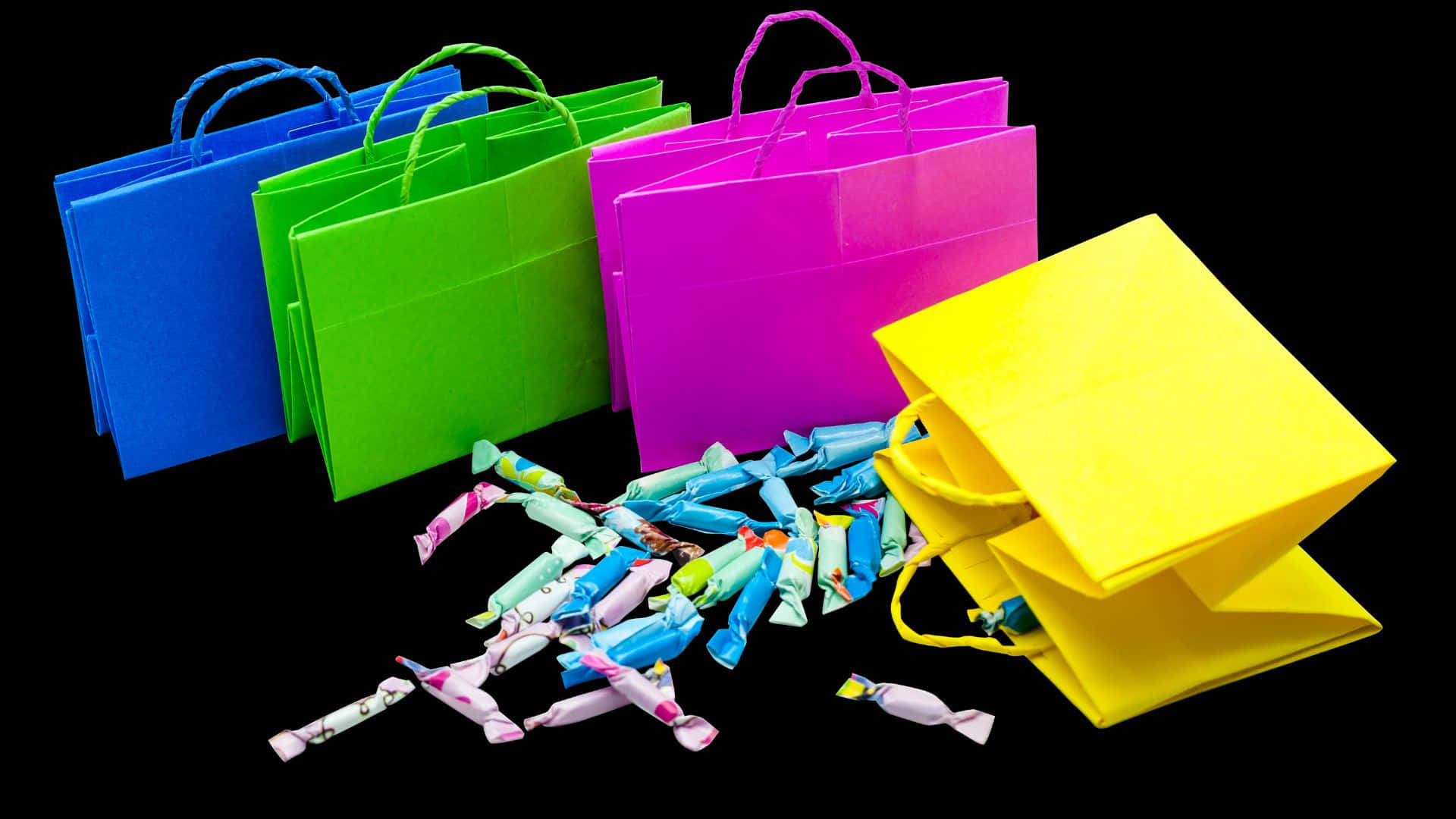 Trick Or Treat Bags 桌布 壁紙 — 色彩繽紛的購物袋和散落的糖果包裝紙在純黑背景上鋪開。